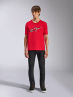 Alpinestars Ageless Shadow CSF Tee, t-shirt a maniche corte, rosso, logo Ageless frontale con contorni bianchi e neri, indossata da un modello con pantaloni neri e sneakers, casual motorsport streetwear