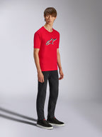 Alpinestars Ageless Shadow CSF Tee, t-shirt rossa a maniche corte, con un grande logo Ageless sul petto, indossata da un modello con pantaloni neri e sneakers, streetwear casual motorsport
