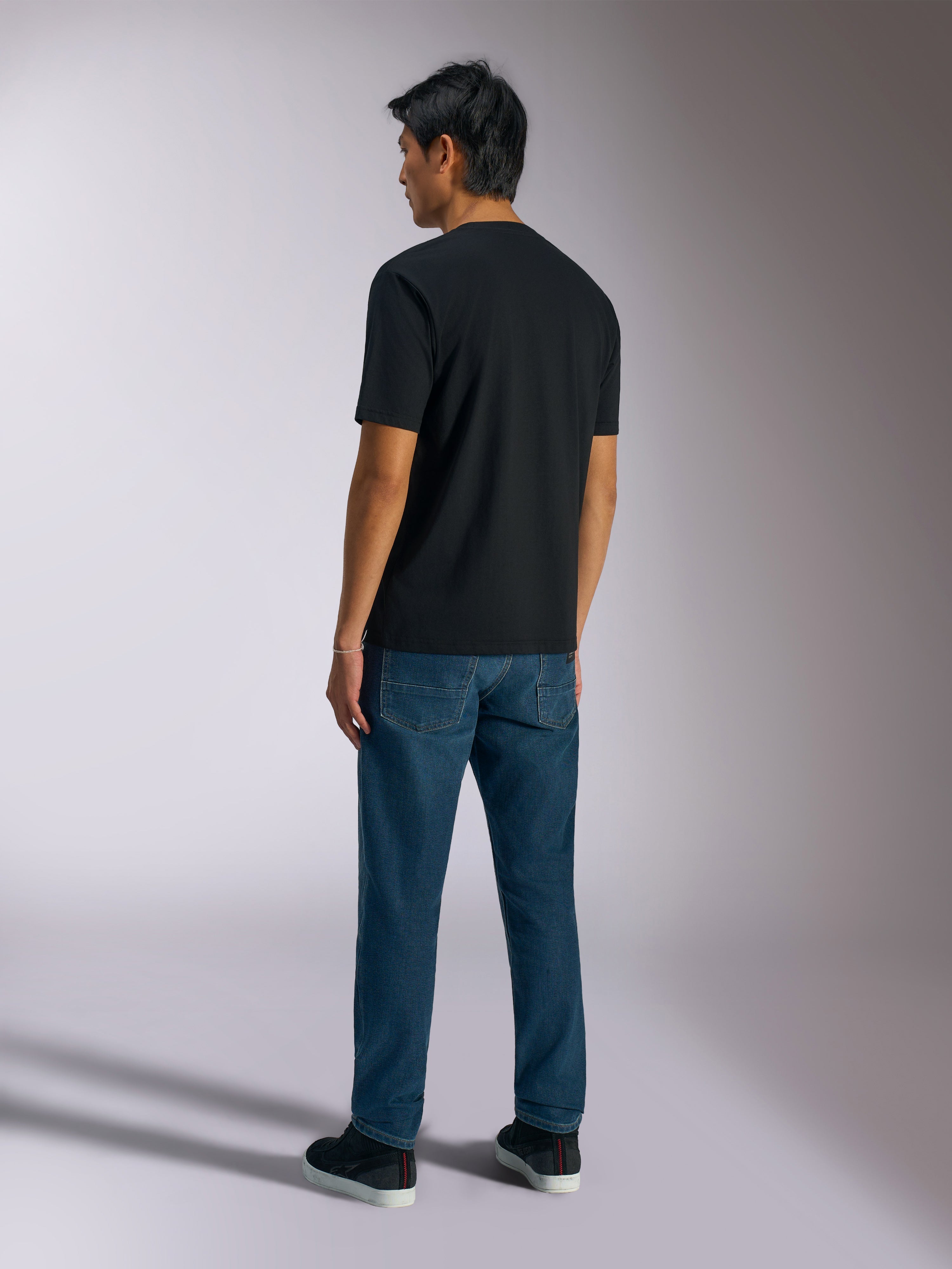 Alpinestars Ageless Shadow CSF Tee, maglietta a maniche corte, nero, vista posteriore, indossata con jeans blu e sneakers nere, streetwear casual ispirato al motorsport