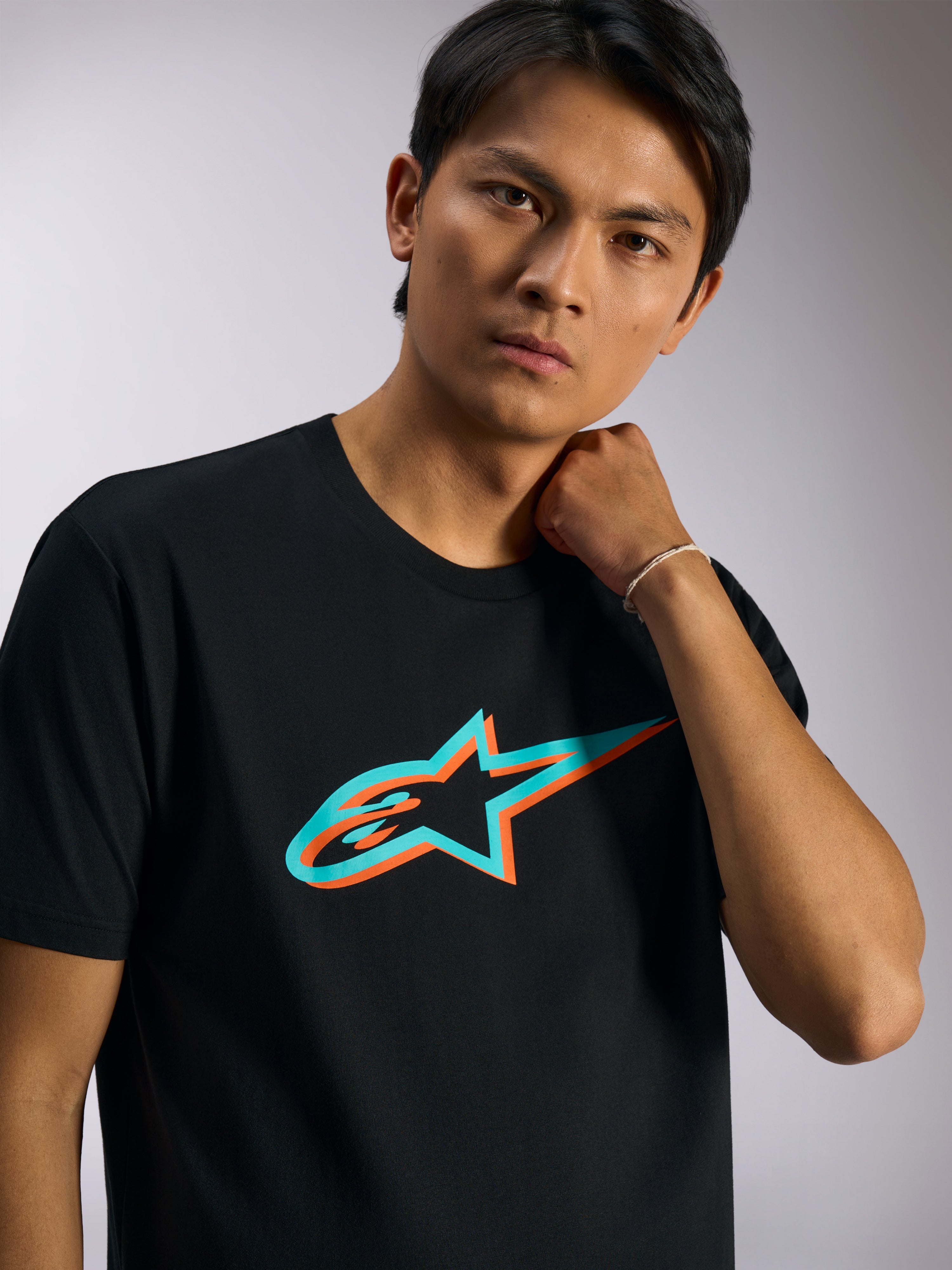 Alpinestars Ageless Shadow CSF Tee, t-shirt a maniche corte, nero con logo in ombra turchese e arancione, indossata da un modello, streetwear casual ispirato al motorsport
