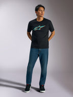 Alpinestars Ageless Shadow CSF Tee, t-shirt a maniche corte, nera, logo Ageless in ombra turchese e arancione sul petto, indossata da un modello con jeans blu e scarpe nere, abbigliamento casual motorsport streetwear