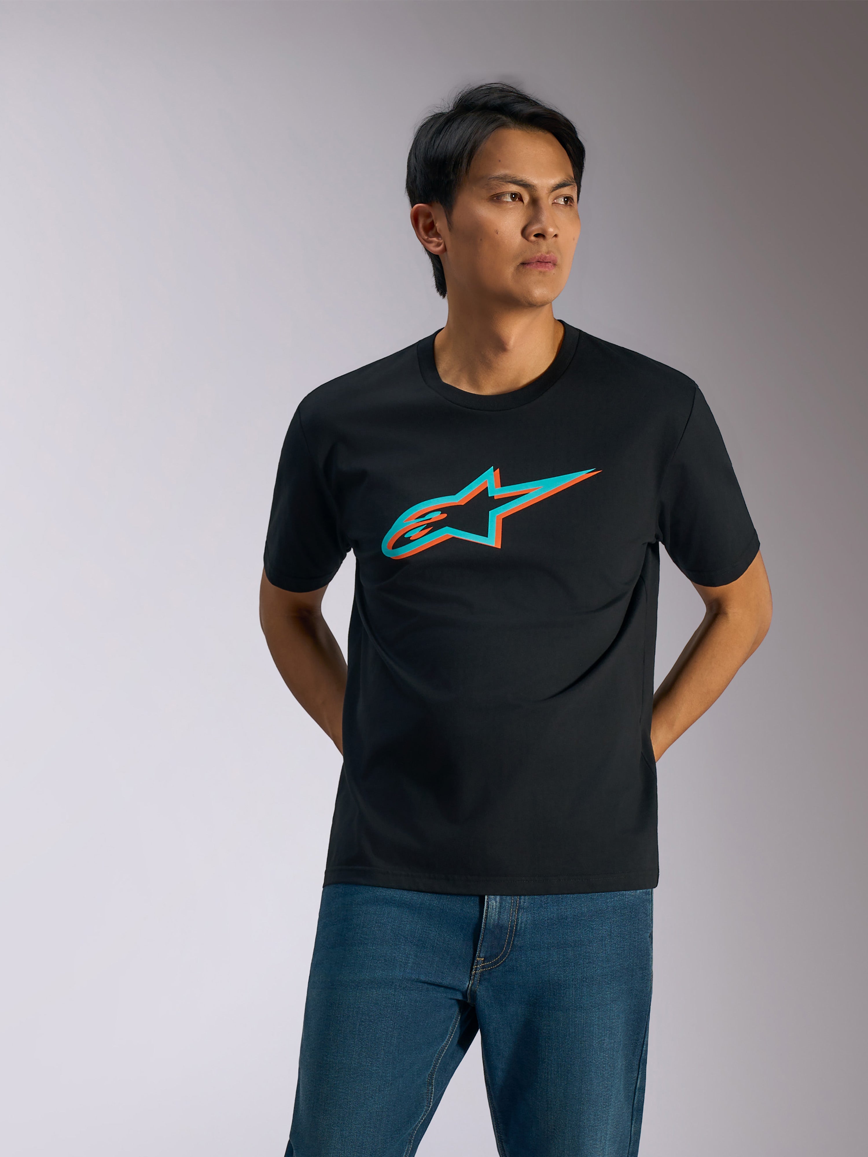 Alpinestars Maglietta Ageless Shadow CSF, t-shirt a maniche corte, nera con logo in ombra turchese e arancione, indossata da un uomo con jeans blu, streetwear casual motorsport