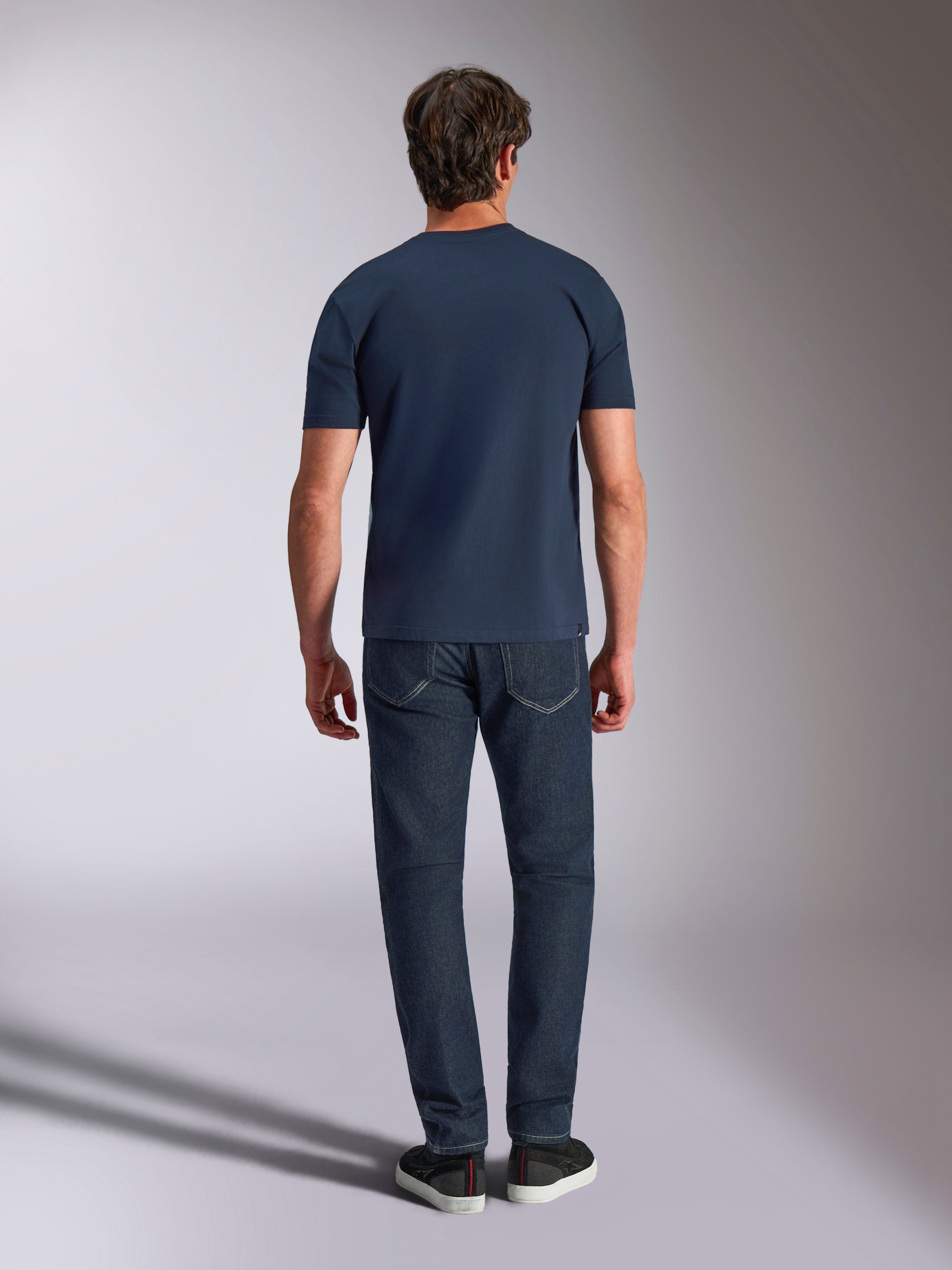 Alpinestars Ageless Shadow CSF Tee, t-shirt a maniche corte, blu navy, vista posteriore di un modello che indossa la t-shirt con jeans scuri e sneakers nere, streetwear casual ispirato al motorsport.