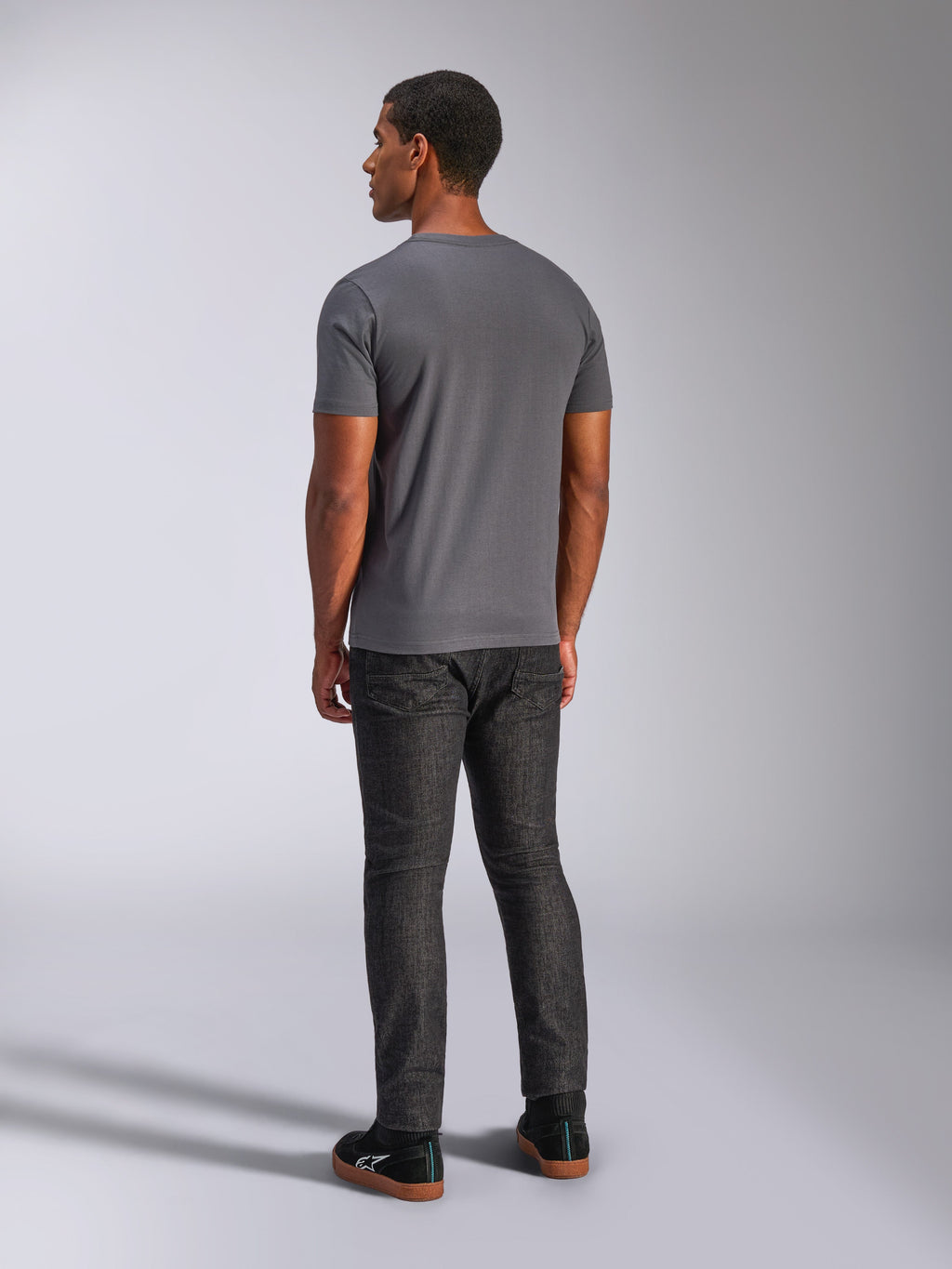 Alpinestars Always 2.0 CSF Tee, t-shirt a maniche corte, grigio antracite, vista posteriore su modello, abbinata a pantaloni in denim scuro e sneakers nere, streetwear casual ispirato al motorsport