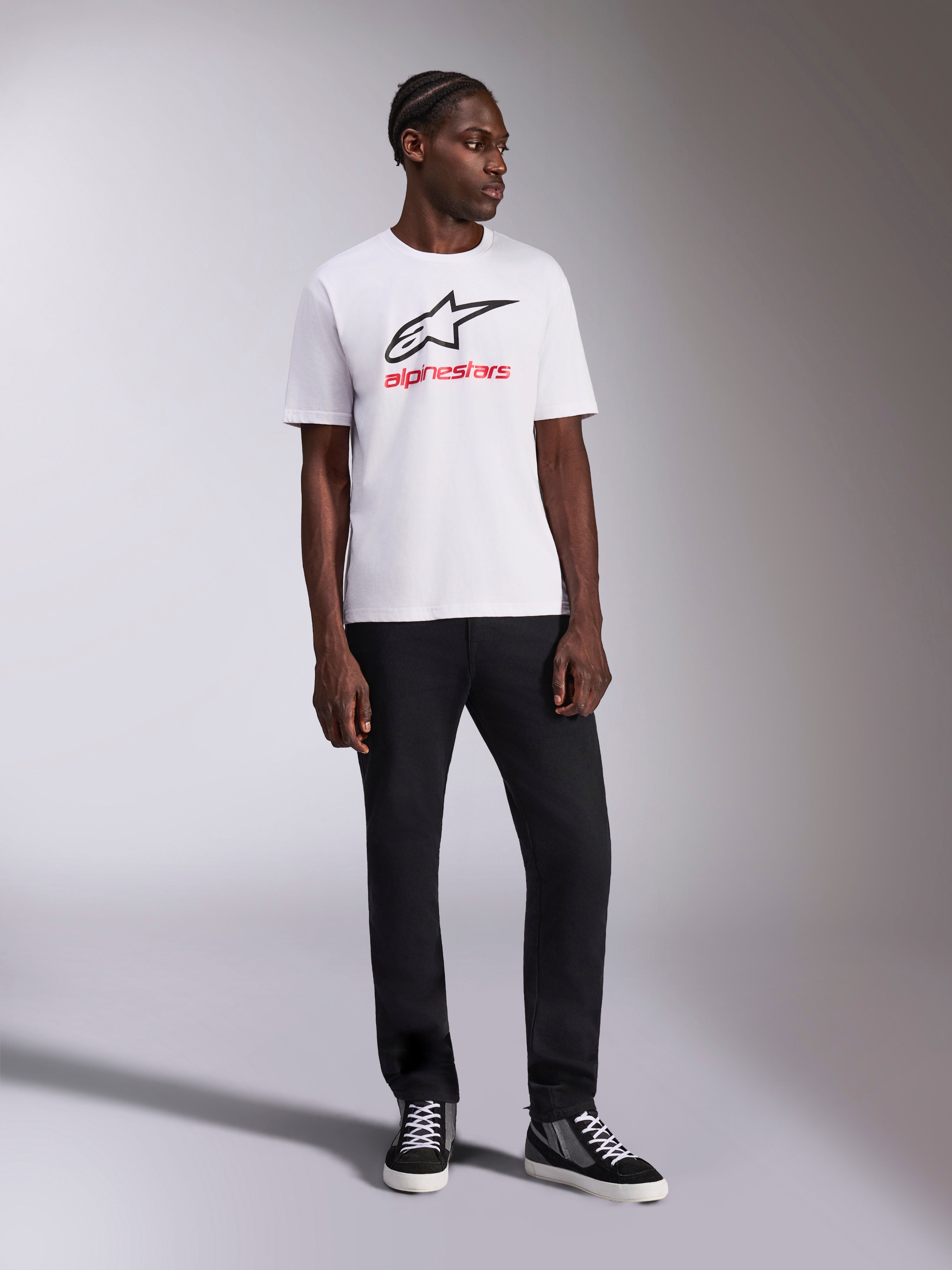Alpinestars Always 2.0 CSF Tee, T-shirt a maniche corte, bianca, logo Astar nero e grafica wordmark Alpinestars rossa, indossata da un modello con pantaloni neri e sneakers alte, abbigliamento sportivo casual motorsport