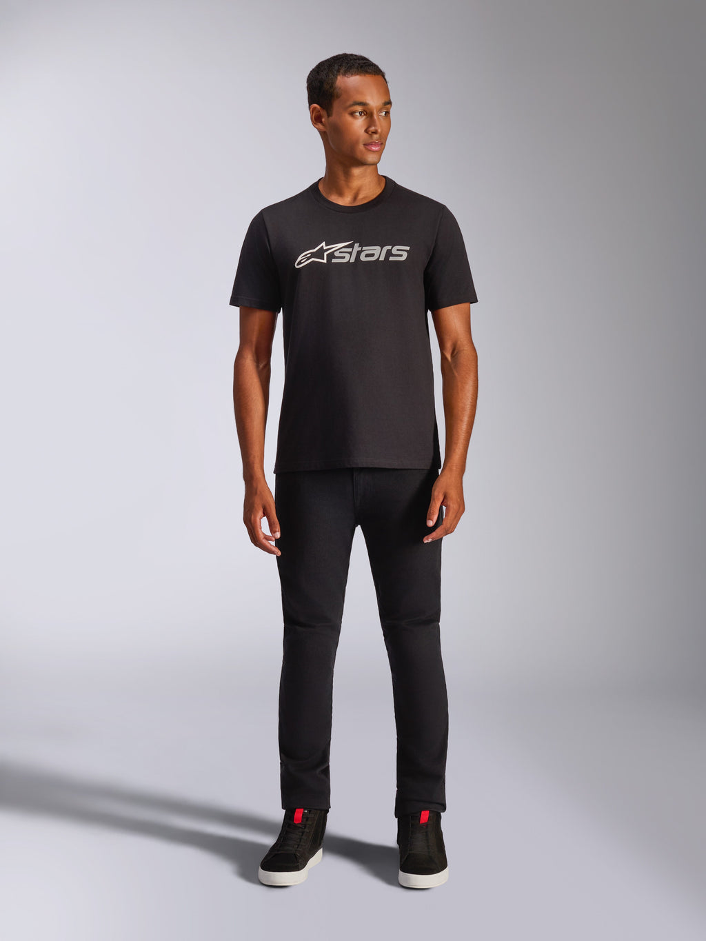 Alpinestars Blaze 2.0 CSF Tee, maglietta a maniche corte, nera con logo frontale grigio e bianco, indossata da un modello con pantaloni neri e scarpe nere, streetwear casual ispirato al motorsport