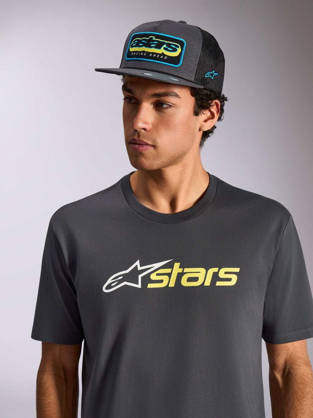 Alpinestars Blaze 2.0 CSF Tee, t-shirt a maniche corte, grigio antracite con logo bianco e giallo alta visibilità, indossata con cappellino coordinato grigio antracite con retro in rete, abbigliamento sportivo casual ispirato al motorsport