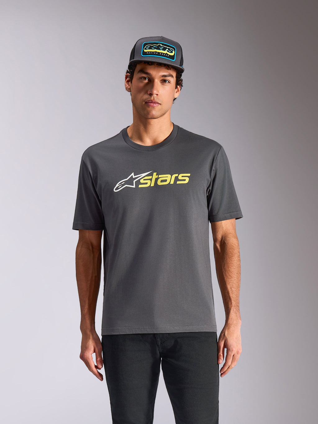 Alpinestars Blaze 2.0 CSF Tee, t-shirt a maniche corte, grigio antracite, logo con stella bianca e grafica "stars" giallo alta visibilità, indossata con cappellino trucker coordinato e pantaloni neri, streetwear casual ispirato al motorsport