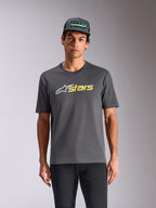 Alpinestars Blaze 2.0 CSF Tee, t-shirt a maniche corte, grigio antracite, logo con stella bianca e grafica "stars" giallo alta visibilità, indossata con cappellino trucker coordinato e pantaloni neri, streetwear casual ispirato al motorsport