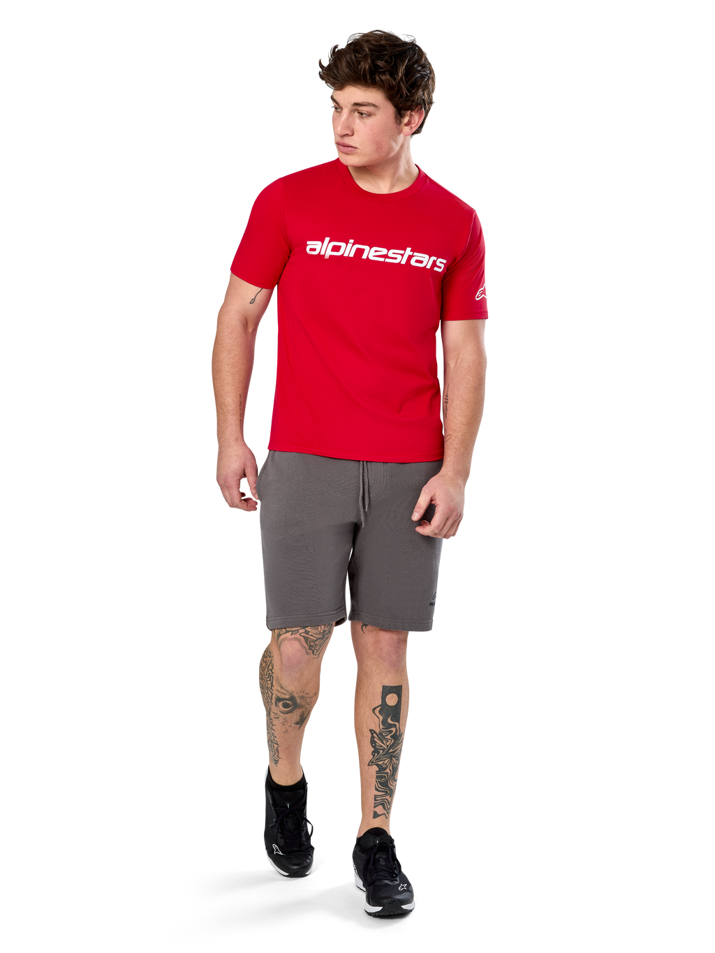 Alpinestars Linear Wordmark 2.0 CSF Tee, t-shirt a maniche corte, rossa con logo wordmark bianco sul petto, indossata da un modello con pantaloncini grigi e sneakers nere, streetwear casual ispirato al motorsport