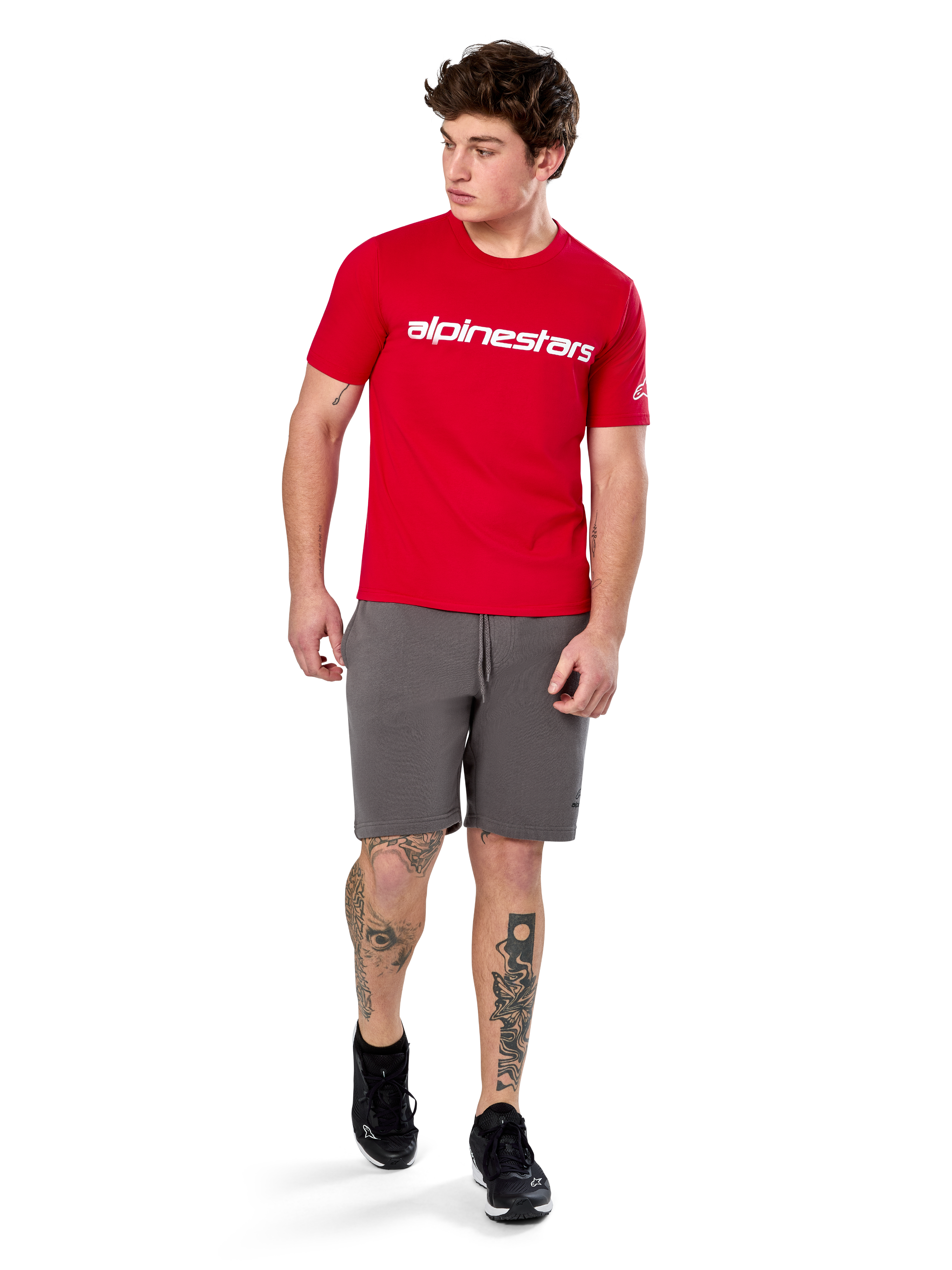 Alpinestars Linear Wordmark 2.0 CSF Tee, t-shirt a maniche corte, rossa con logo wordmark bianco sul petto, indossata da un modello con pantaloncini grigi e sneakers nere, streetwear casual ispirato al motorsport
