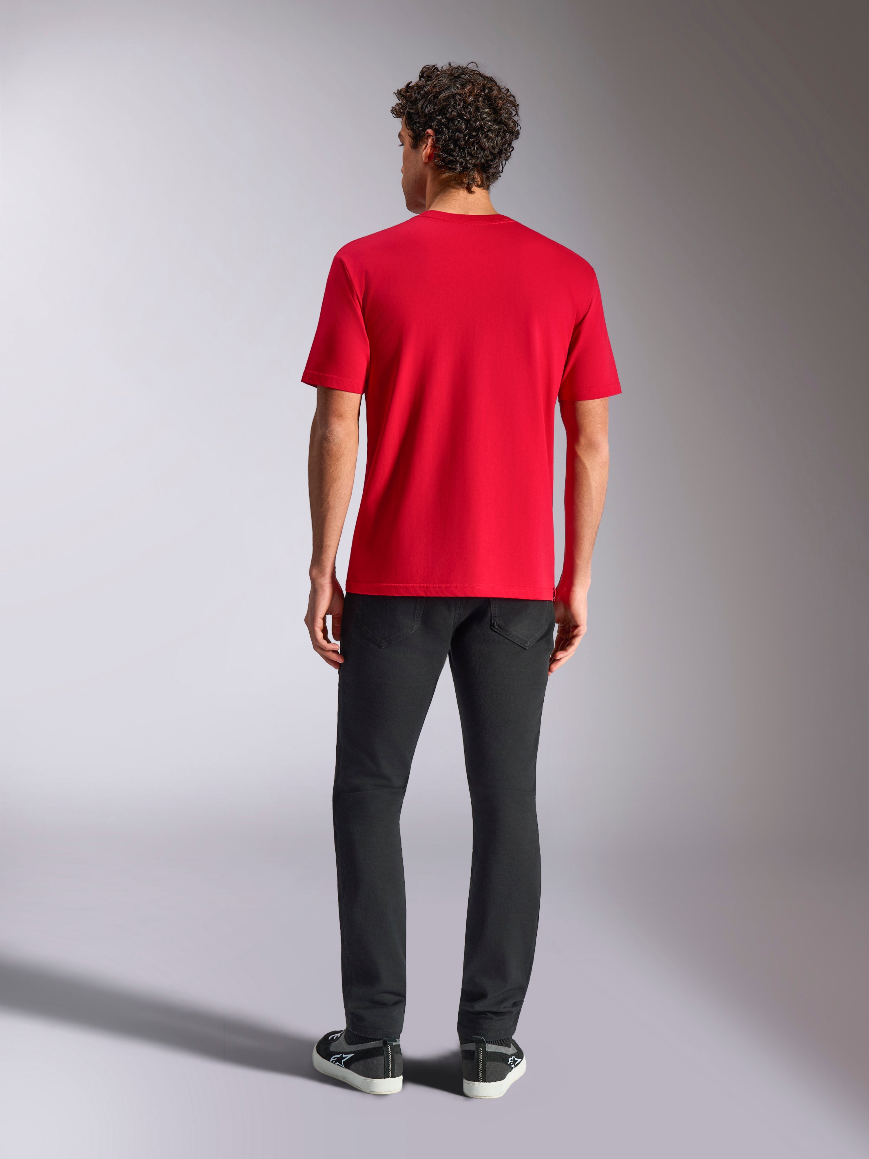 Alpinestars Ride 4.0 CSF Tee, T-shirt a maniche corte, rosso, vista posteriore, indossata con pantaloni neri e sneakers nere, streetwear casual a tema motorsport