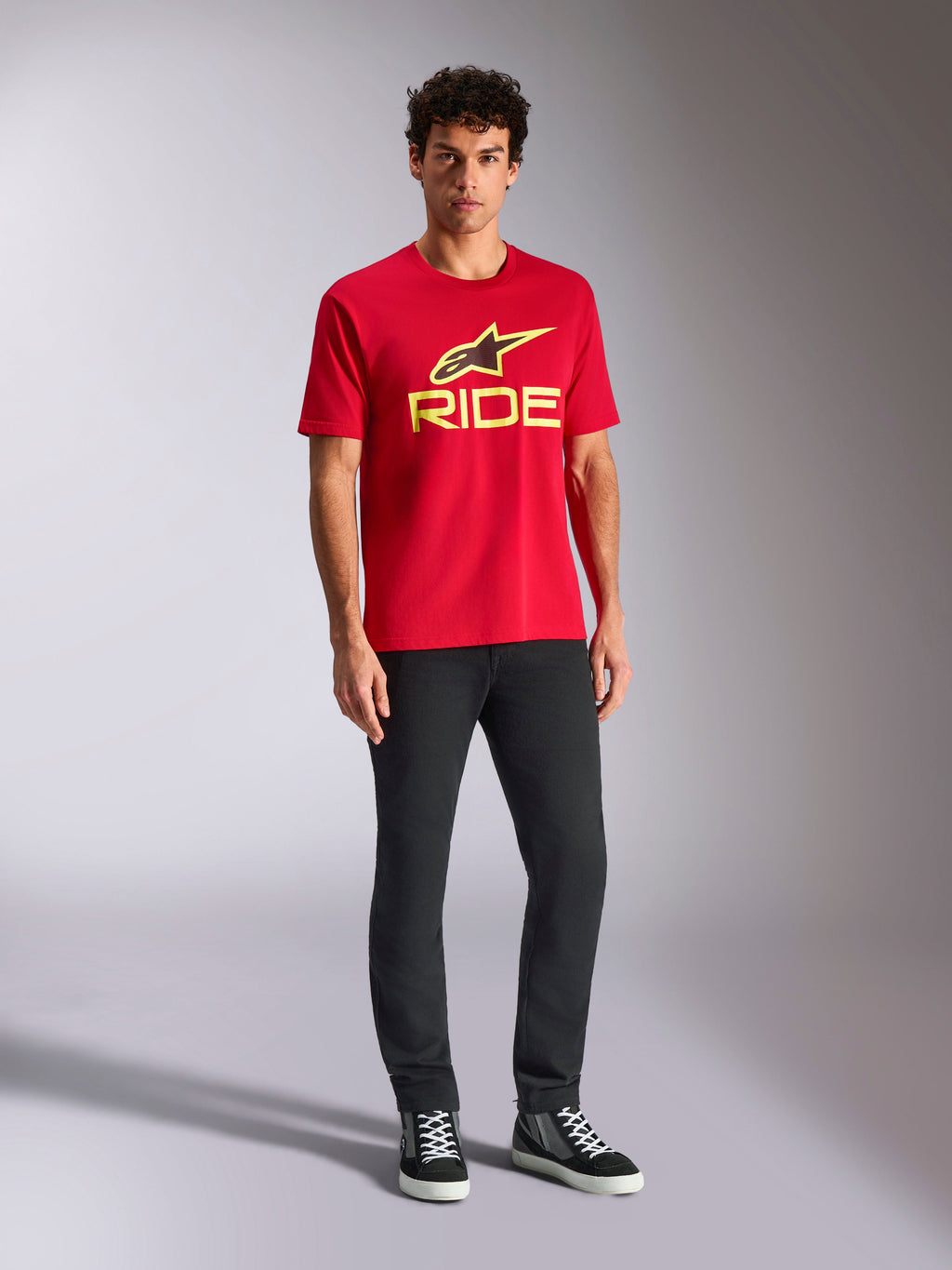 Alpinestars Ride 4.0 CSF Tee, t-shirt a maniche corte, rossa con logo Alpinestars Star e Ride in giallo fluo, indossata da un modello con pantaloni neri e sneakers, abbigliamento sportivo casual motorsport