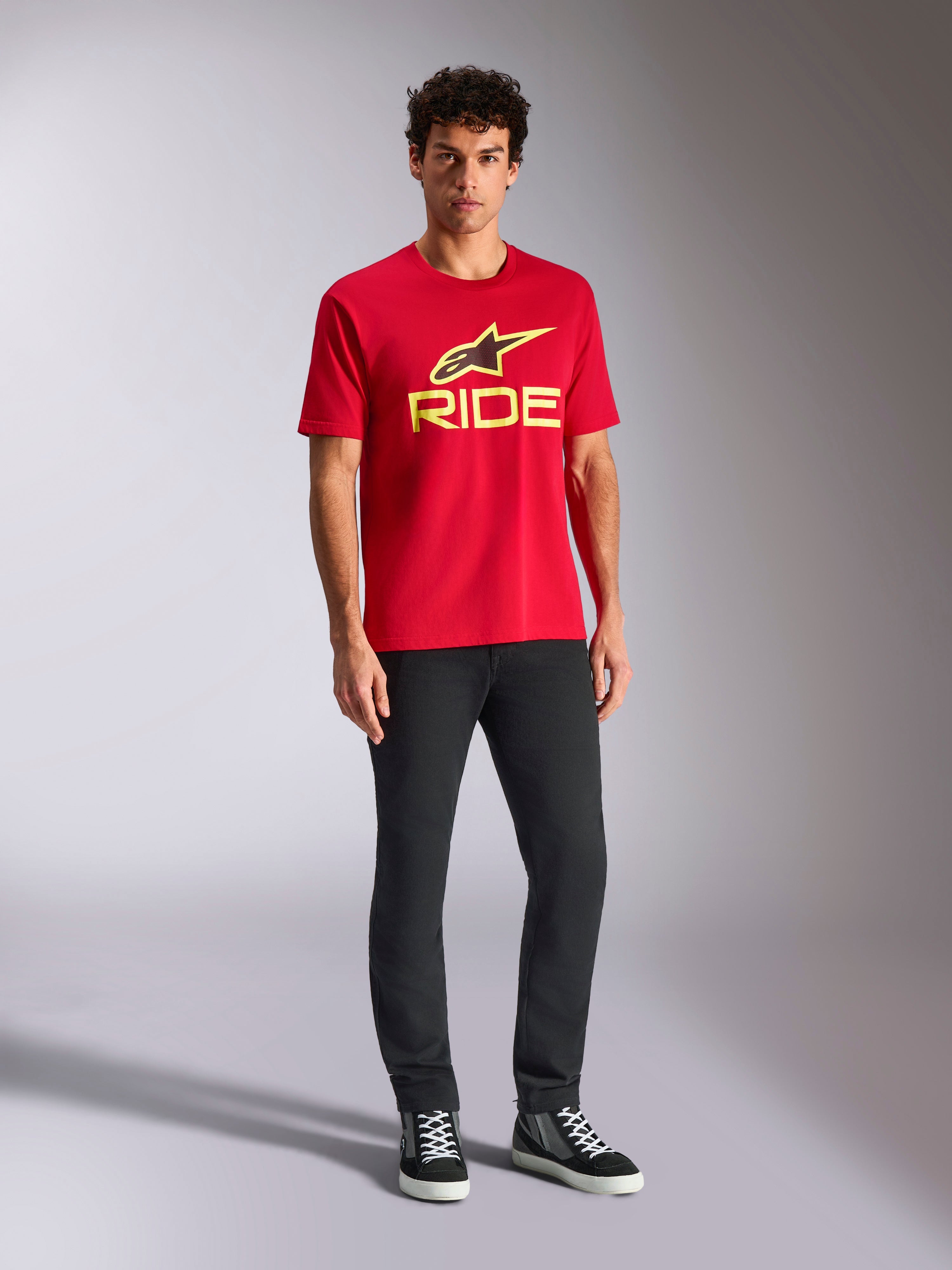 Alpinestars Ride 4.0 CSF Tee, t-shirt a maniche corte, rossa con logo Alpinestars Star e Ride in giallo fluo, indossata da un modello con pantaloni neri e sneakers, abbigliamento sportivo casual motorsport