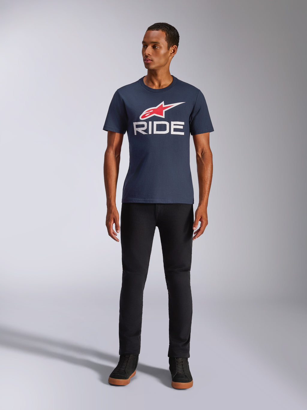 Alpinestars Ride 4.0 CSF Tee, t-shirt a maniche corte, blu navy con logo Alpinestars a stella rosso e scritta 'RIDE' bianca sul petto, indossata da un modello con pantaloni neri e sneaker nere, streetwear casual ispirato al motorsport