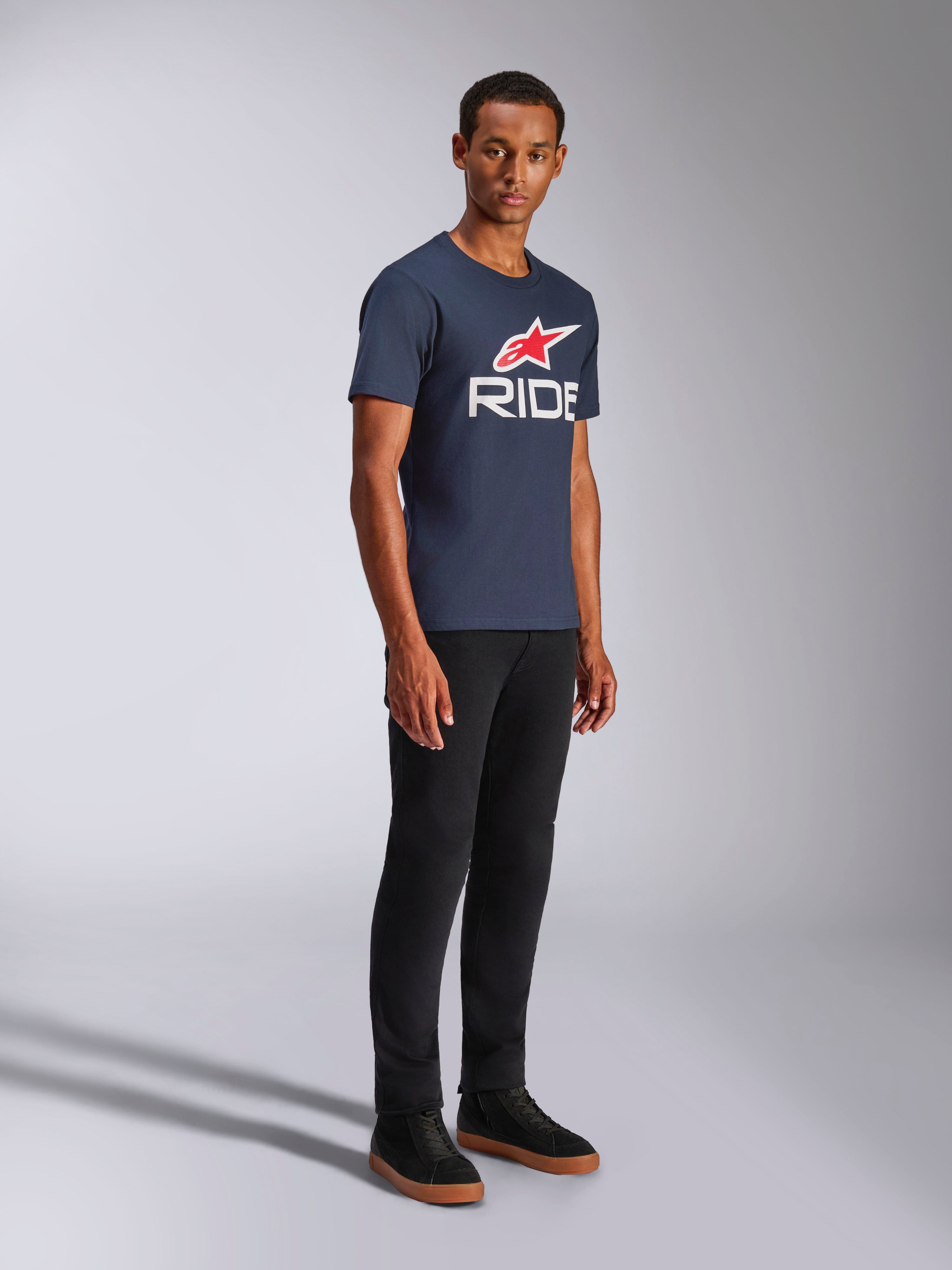 Alpinestars Ride 4.0 CSF Tee, maglietta a maniche corte, blu navy, logo RIDE bianco con stella Alpinestars rossa, indossata da un modello con pantaloni neri e sneakers, abbigliamento casual lifestyle motorsport
