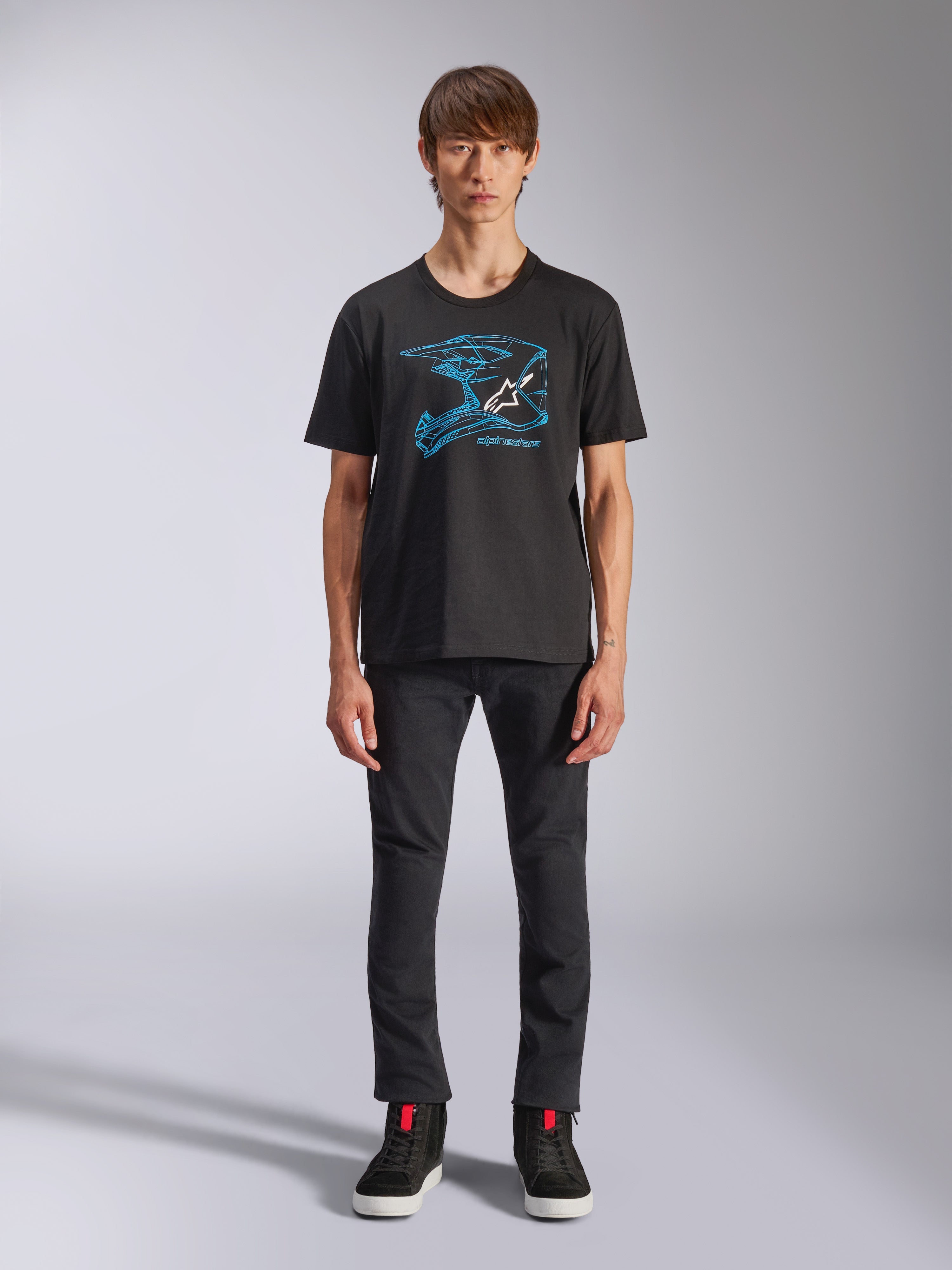 Alpinestars CSF Tee, t-shirt a maniche corte, nero, grafica blu del casco da motocross con logo bianco, indossata da un modello con pantaloni neri e sneakers nere, streetwear casual ispirato al motorsport