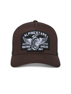 Cappello Alpinestars Heritage Patch Trucker, marrone con rete nera, visiera curva e corona strutturata, grande patch ricamata con ruota alata e grafica "Racing Ahead", copricapo casual ispirato al motorsport