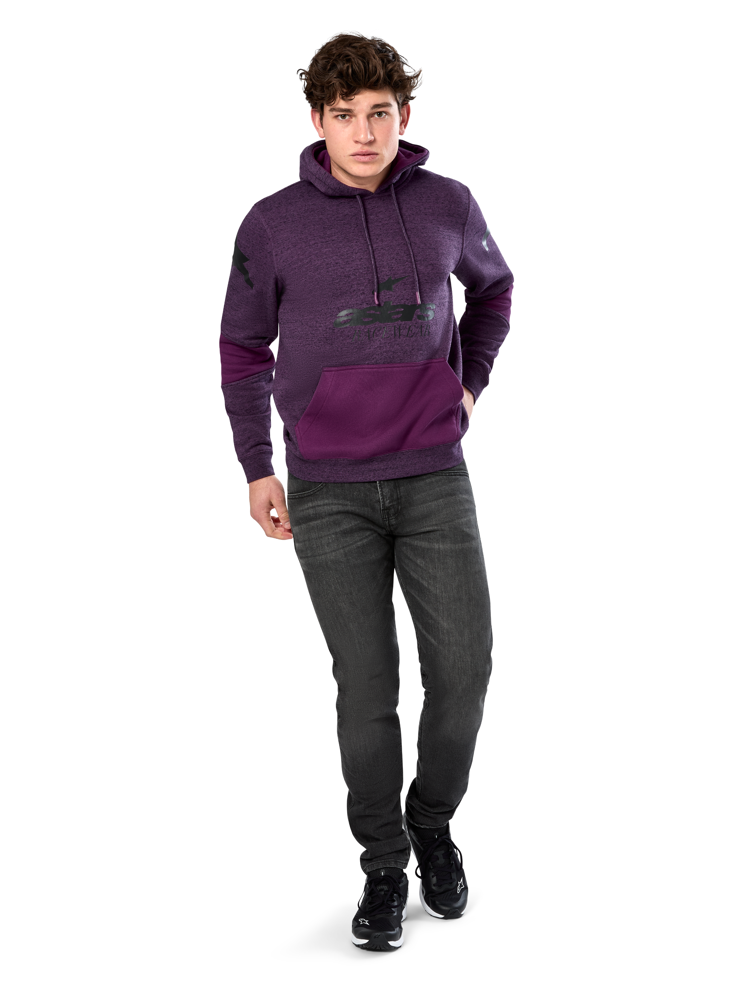 Alpinestars Perpetuate Hoodie, felpa con cappuccio, streetwear casual, pile viola mélange con inserti in tessuto viola scuro sulla tasca a marsupio e sulle maniche, logo nero sul petto, cappuccio con cordino, indossata da un modello con jeans grigio scuro e sneakers nere