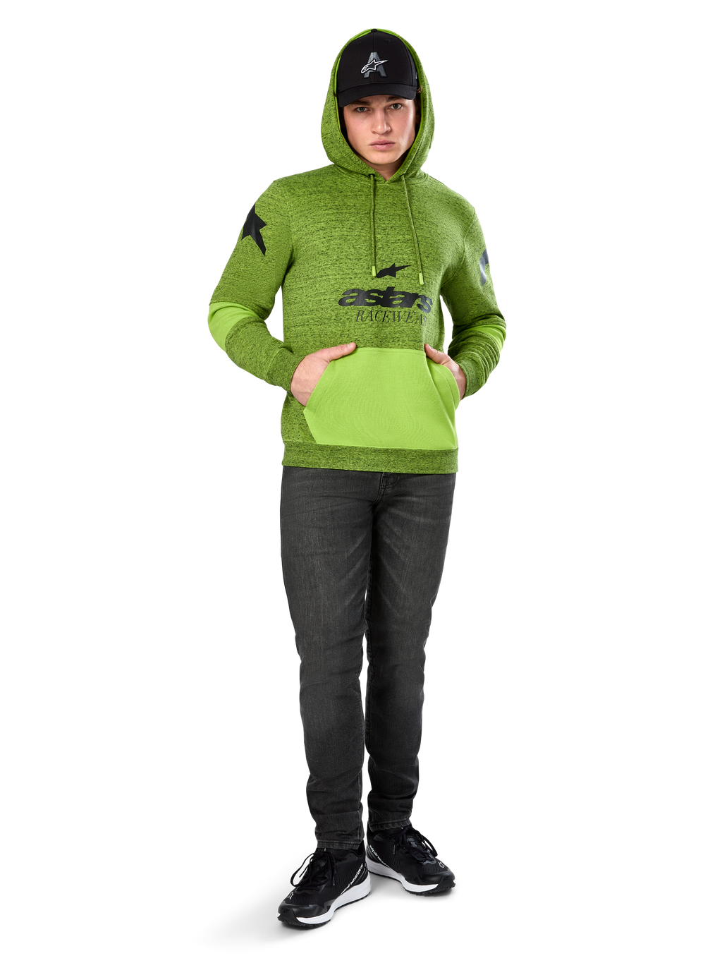 Alpinestars Perpetuate Hoodie, pile mélange verde lime con tasca a marsupio e pannelli sulle maniche in verde brillante a contrasto, grafica frontale 'astars' nera, abbinata a cappellino nero e jeans scuri, streetwear casual ispirato al motorsport