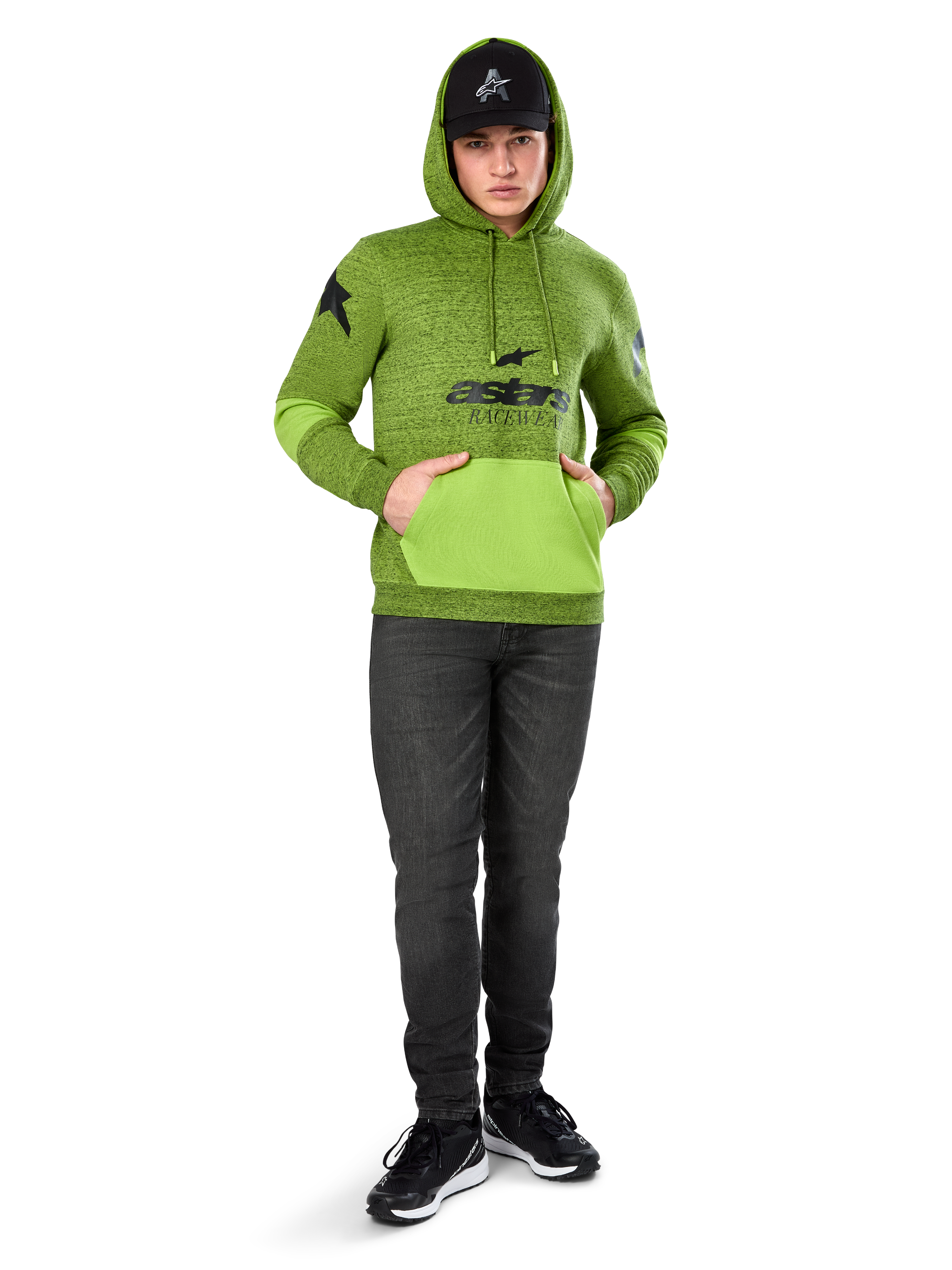 Alpinestars Perpetuate Hoodie, pile mélange verde lime con tasca a marsupio e pannelli sulle maniche in verde brillante a contrasto, grafica frontale 'astars' nera, abbinata a cappellino nero e jeans scuri, streetwear casual ispirato al motorsport