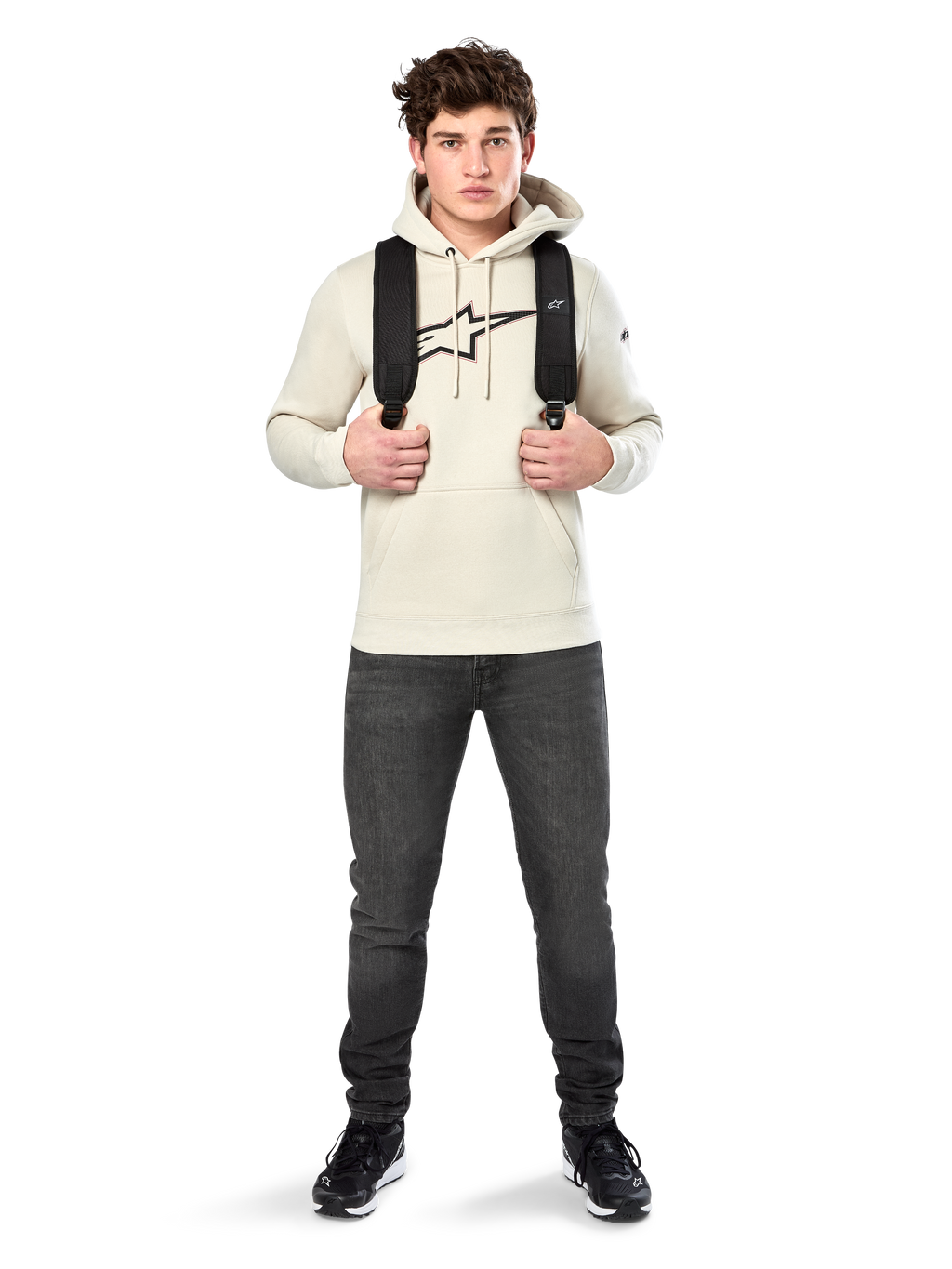 Felpa con cappuccio Alpinestars Insignia, streetwear casual, pullover in pile Off White, logo effetto fibra di carbonio con bordo rosso, cappuccio con cordino, tasca a marsupio, indossata da un modello con zaino nero e jeans grigio scuro