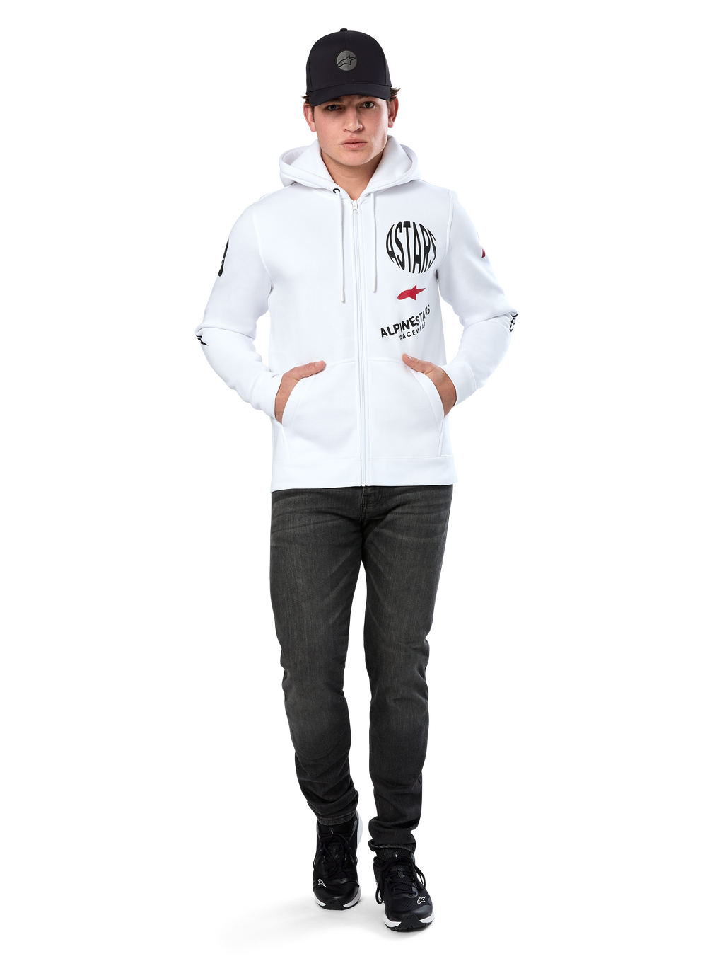 Felpa con cappuccio Alpinestars Variegate, felpa in pile bianca con zip, grafica multi-logo con scritta 'ASTARS' e logo a stella rosso sul petto, dettagli grafici sulle maniche, indossata da un modello con cappellino nero e jeans neri, abbigliamento streetwear casual motorsport