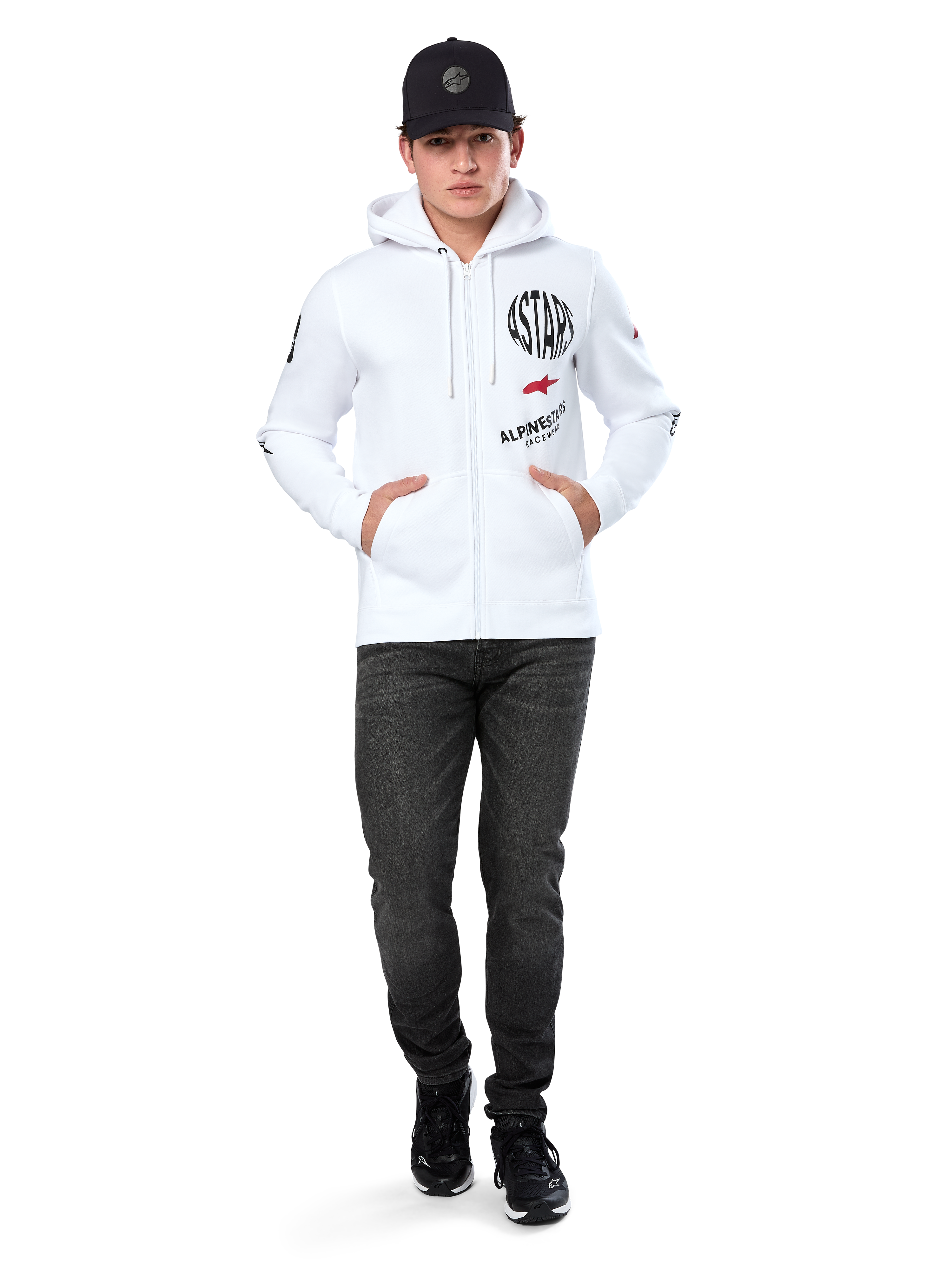 Felpa con cappuccio Alpinestars Variegate, felpa in pile bianca con zip, grafica multi-logo con scritta 'ASTARS' e logo a stella rosso sul petto, dettagli grafici sulle maniche, indossata da un modello con cappellino nero e jeans neri, abbigliamento streetwear casual motorsport