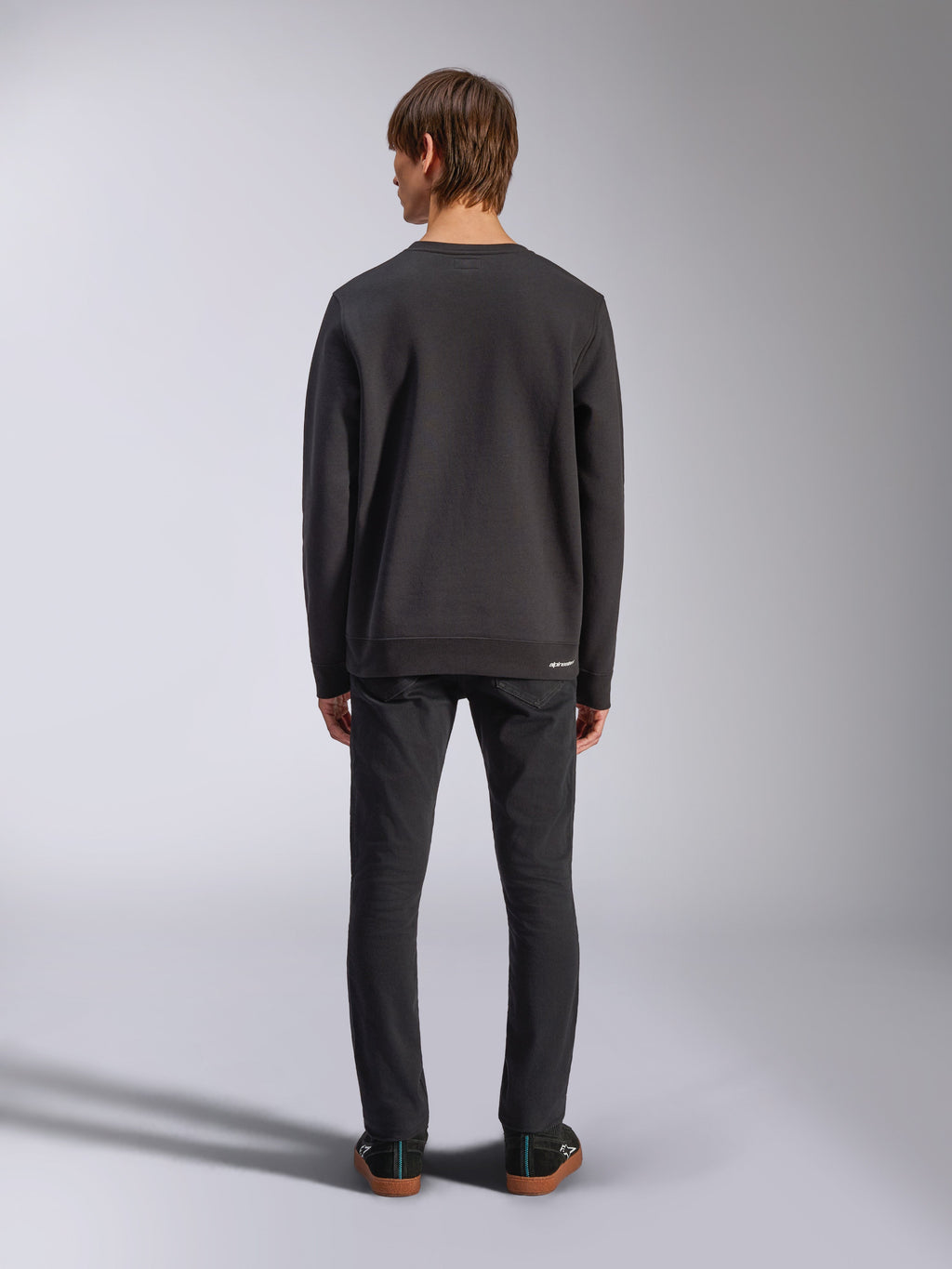Alpinestars Positive Crew, felpa nera, vista posteriore su modello, indossata con jeans neri e sneakers casual, con polsini e orlo a coste, streetwear ispirato al motorsport