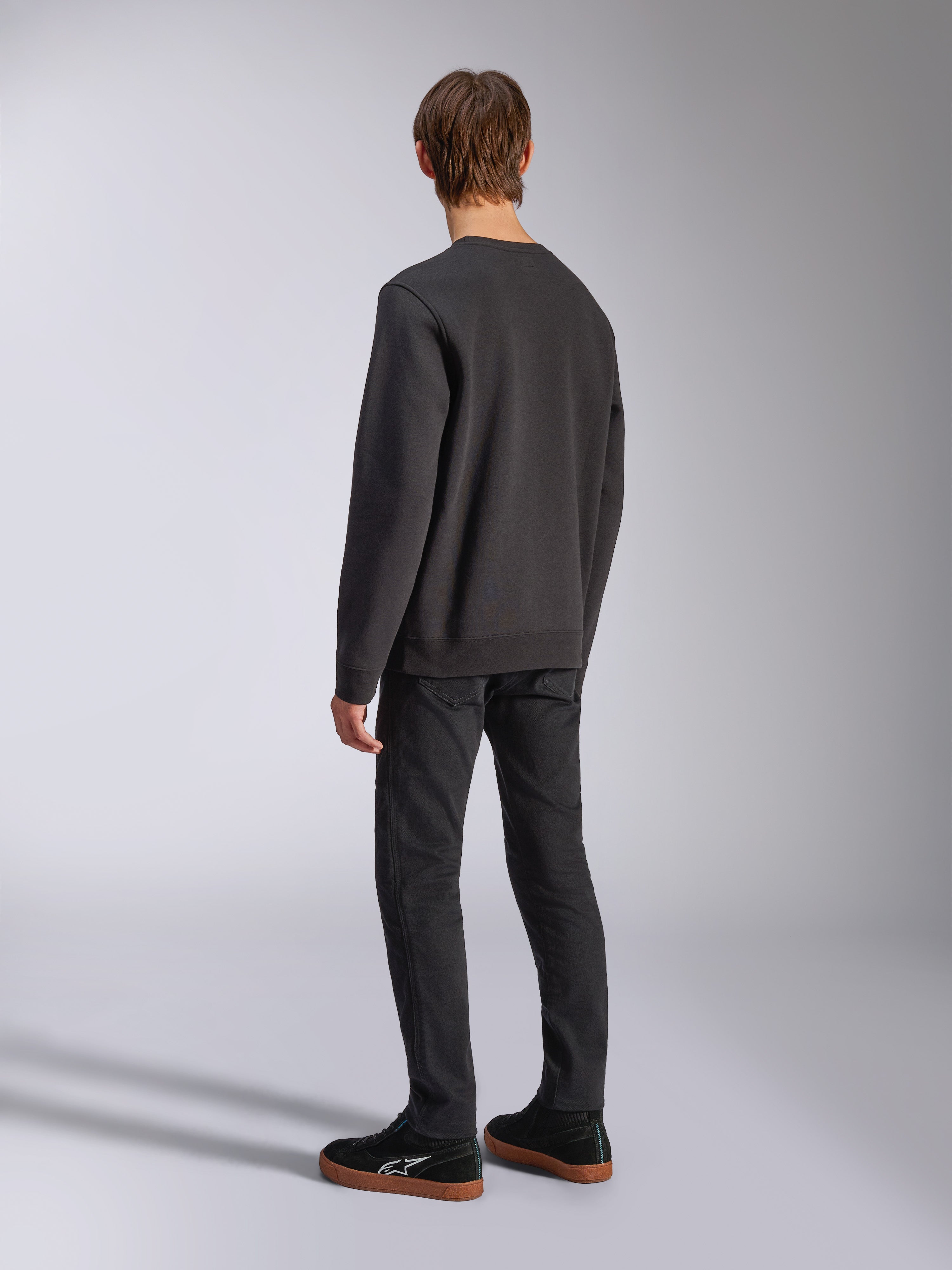 Alpinestars Positive Crew, felpa nera girocollo, vista posteriore su modello, streetwear casual ispirato al motorsport, con orlo e polsini a coste.