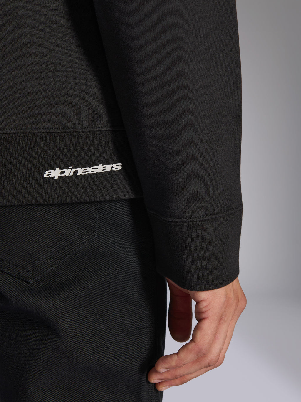 Alpinestars Positive Crew, felpa girocollo nera, dettaglio ravvicinato dell'orlo a coste e del polsino con logo Alpinestars bianco, trama del tessuto premium, abbigliamento sportivo casual ispirato al motorsport