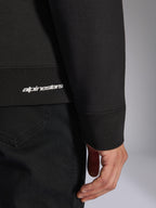 Alpinestars Positive Crew, felpa girocollo nera, dettaglio ravvicinato dell'orlo a coste e del polsino con logo Alpinestars bianco, trama del tessuto premium, abbigliamento sportivo casual ispirato al motorsport