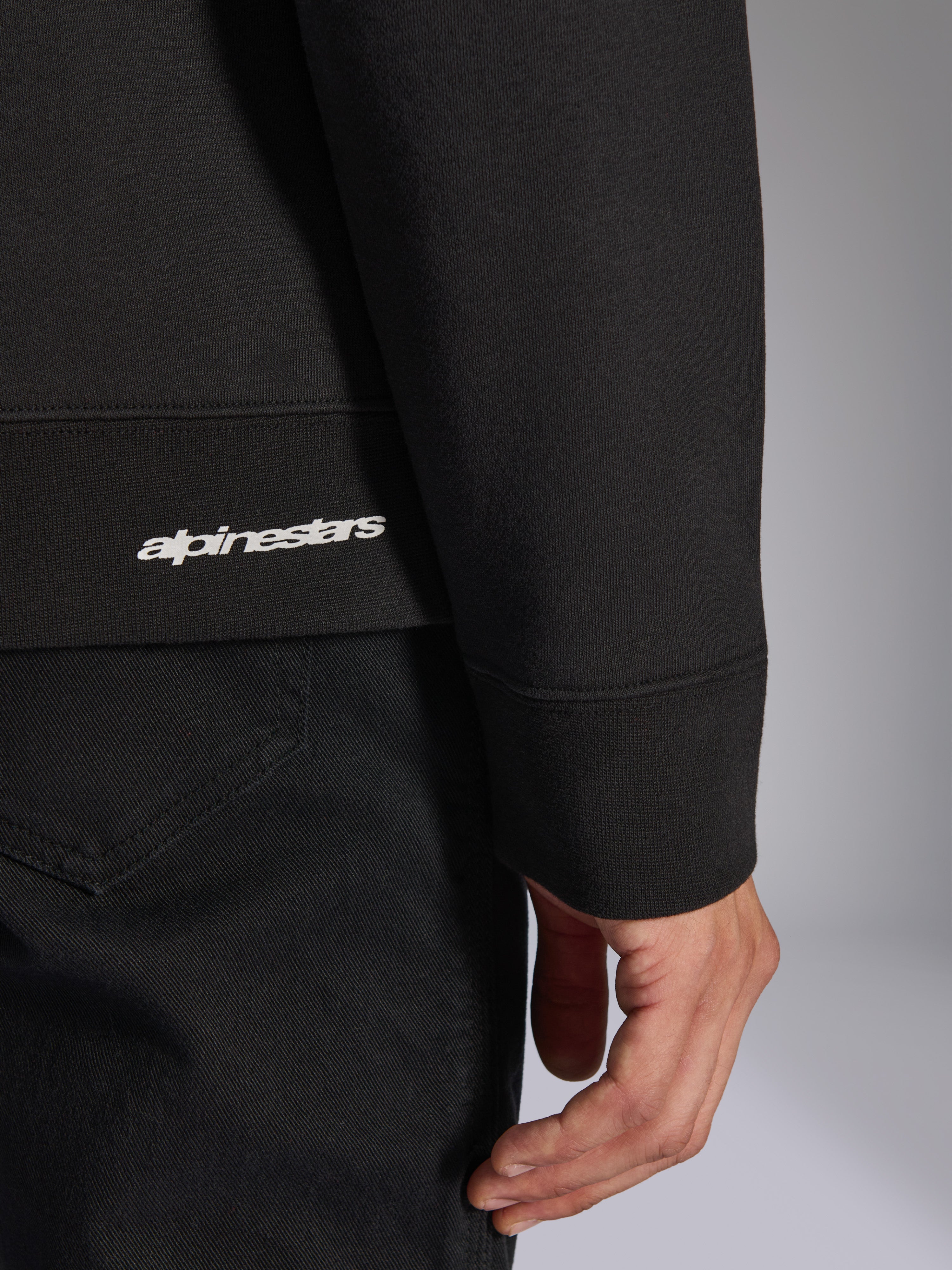 Alpinestars Positive Crew, felpa girocollo nera, dettaglio ravvicinato dell'orlo a coste e del polsino con logo Alpinestars bianco, trama del tessuto premium, abbigliamento sportivo casual ispirato al motorsport