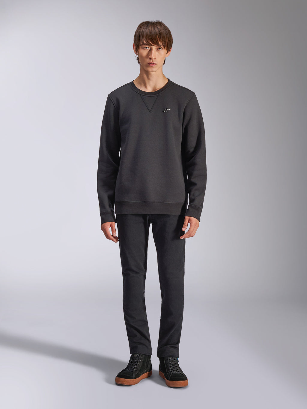 Alpinestars Positive Crew Sweatshirt, felpa girocollo casual nera, piccolo logo bianco sul petto, scollo con cucitura a V, foto a figura intera in studio con modello che indossa pantaloni e sneaker neri, abbigliamento lifestyle ispirato al motorsport