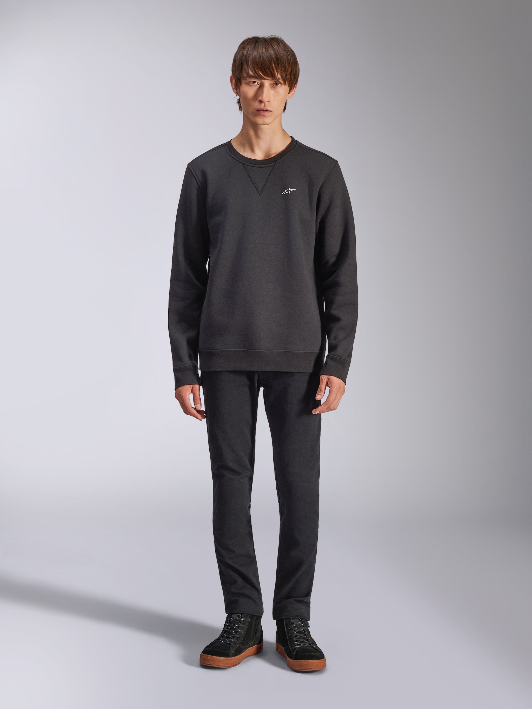 Alpinestars Positive Crew Sweatshirt, Casual Black Crewneck, Small White Logo on Chest, V-stitch Neckline, Full-Body Studio Shot with Model wearing Black Pants and Sneakers, Motorsport-Inspired Lifestyle Apparel