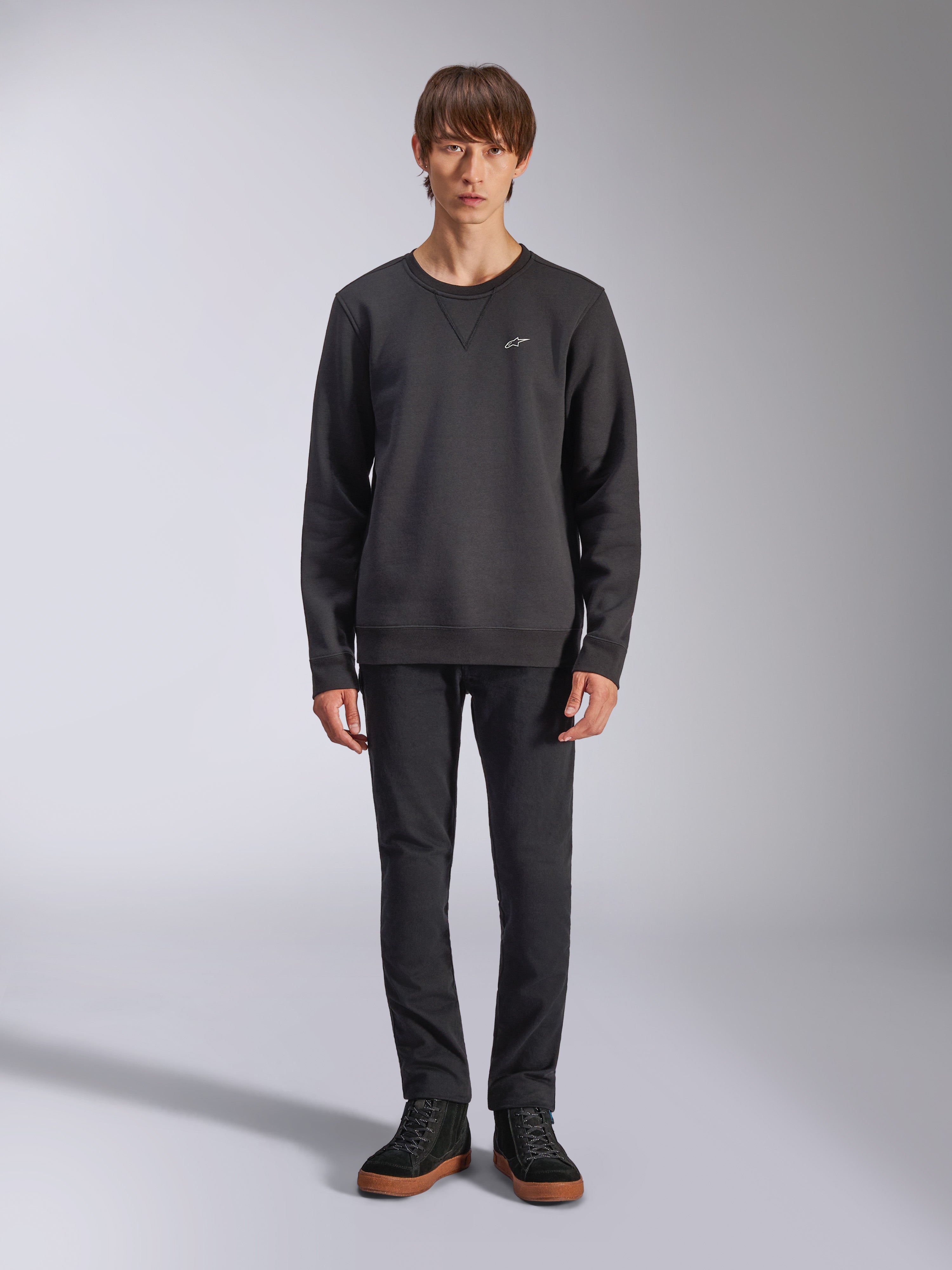 Alpinestars Positive Crew Sweatshirt, felpa girocollo casual nera, piccolo logo bianco sul petto, scollo con cucitura a V, foto a figura intera in studio con modello che indossa pantaloni e sneaker neri, abbigliamento lifestyle ispirato al motorsport