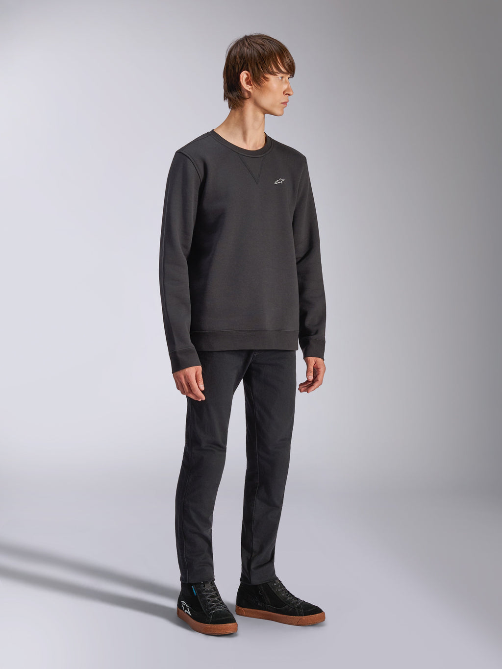 Alpinestars Positive Crew, felpa girocollo, nera, piccolo logo Alpinestars bianco sul petto, colletto a costine con cucitura a V, polsini e orlo a costine, indossata da un modello con pantaloni neri e sneakers, streetwear casual ispirato al motorsport