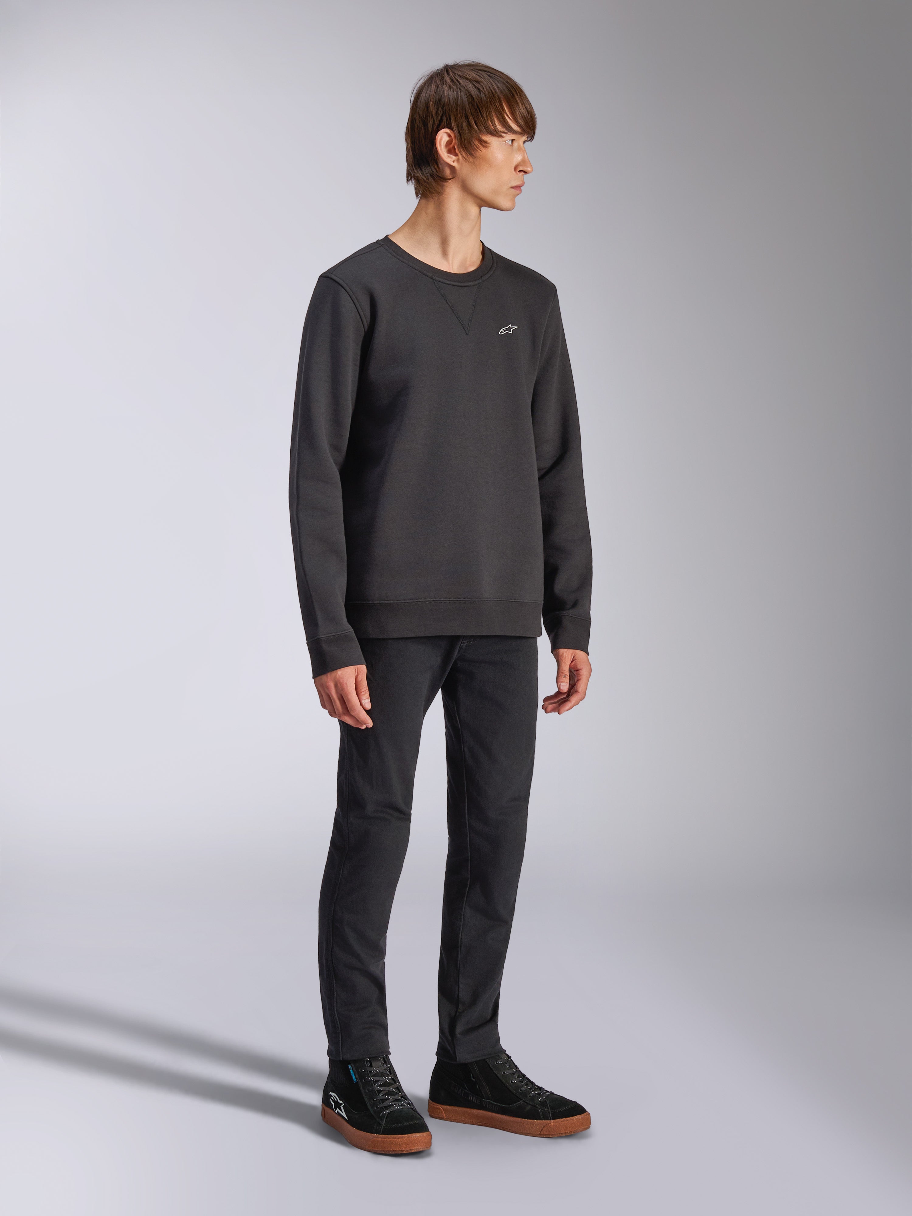 Alpinestars Positive Crew, felpa girocollo, nera, piccolo logo Alpinestars bianco sul petto, colletto a costine con cucitura a V, polsini e orlo a costine, indossata da un modello con pantaloni neri e sneakers, streetwear casual ispirato al motorsport