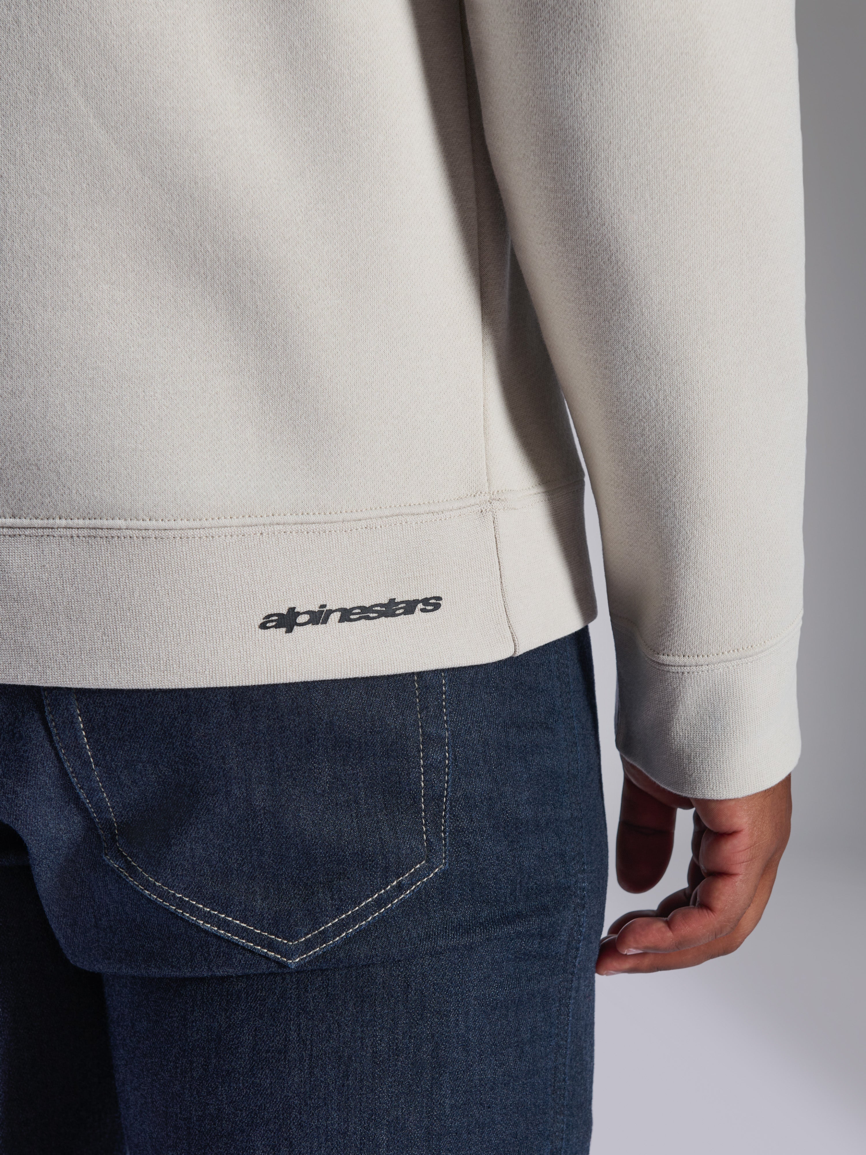 Felpa Alpinestars Positive Crew, Off White, dettaglio ravvicinato di orlo e polsino a coste, con piccolo logo Alpinestars nero, abbigliamento casual ispirato al motorsport