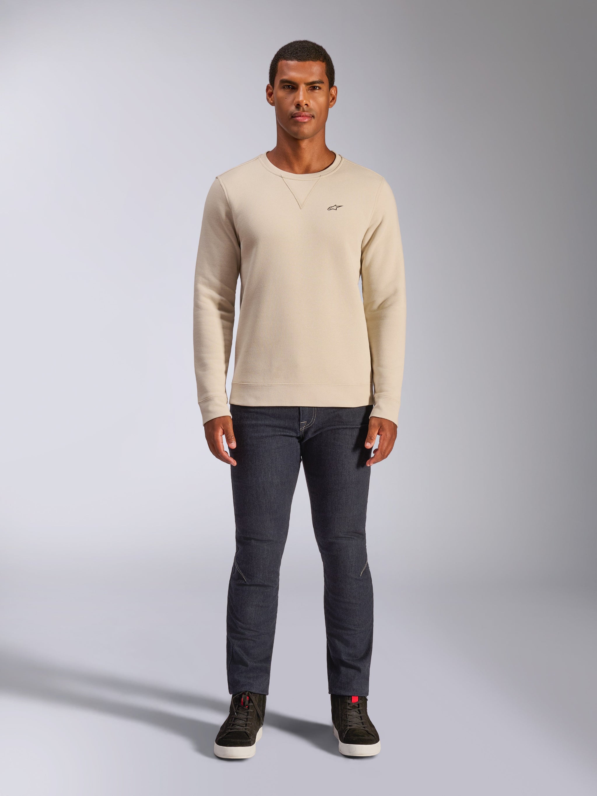 Alpinestars Positive Crew, felpa girocollo Off White, piccolo logo nero sul petto, polsini e orlo a coste, cucitura a triangolo sul collo, streetwear casual motorsport indossata con jeans scuri