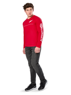 Alpinestars Committed CSF Tee, maglietta a maniche lunghe, rossa, con logo Astars bianco sul petto e marchio Alpinestars sulla manica, indossata da un modello con jeans scuri e sneakers nere, streetwear casual motorsport