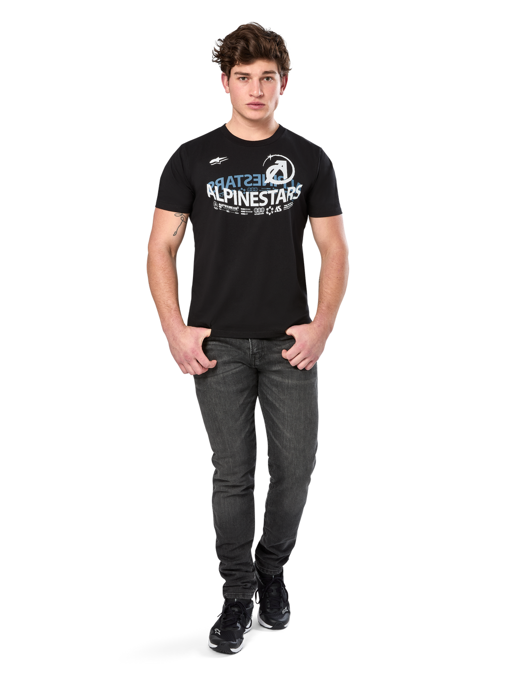 Alpinestars Semicircle CSF Tee, maglietta a maniche corte, nera, grafica curva bianca e azzurra sul petto, indossata da un modello con jeans grigio scuro e sneakers nere, streetwear casual da motorsport