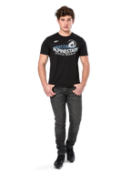 Alpinestars Semicircle CSF Tee, maglietta a maniche corte, nera, grafica curva bianca e azzurra sul petto, indossata da un modello con jeans grigio scuro e sneakers nere, streetwear casual da motorsport
