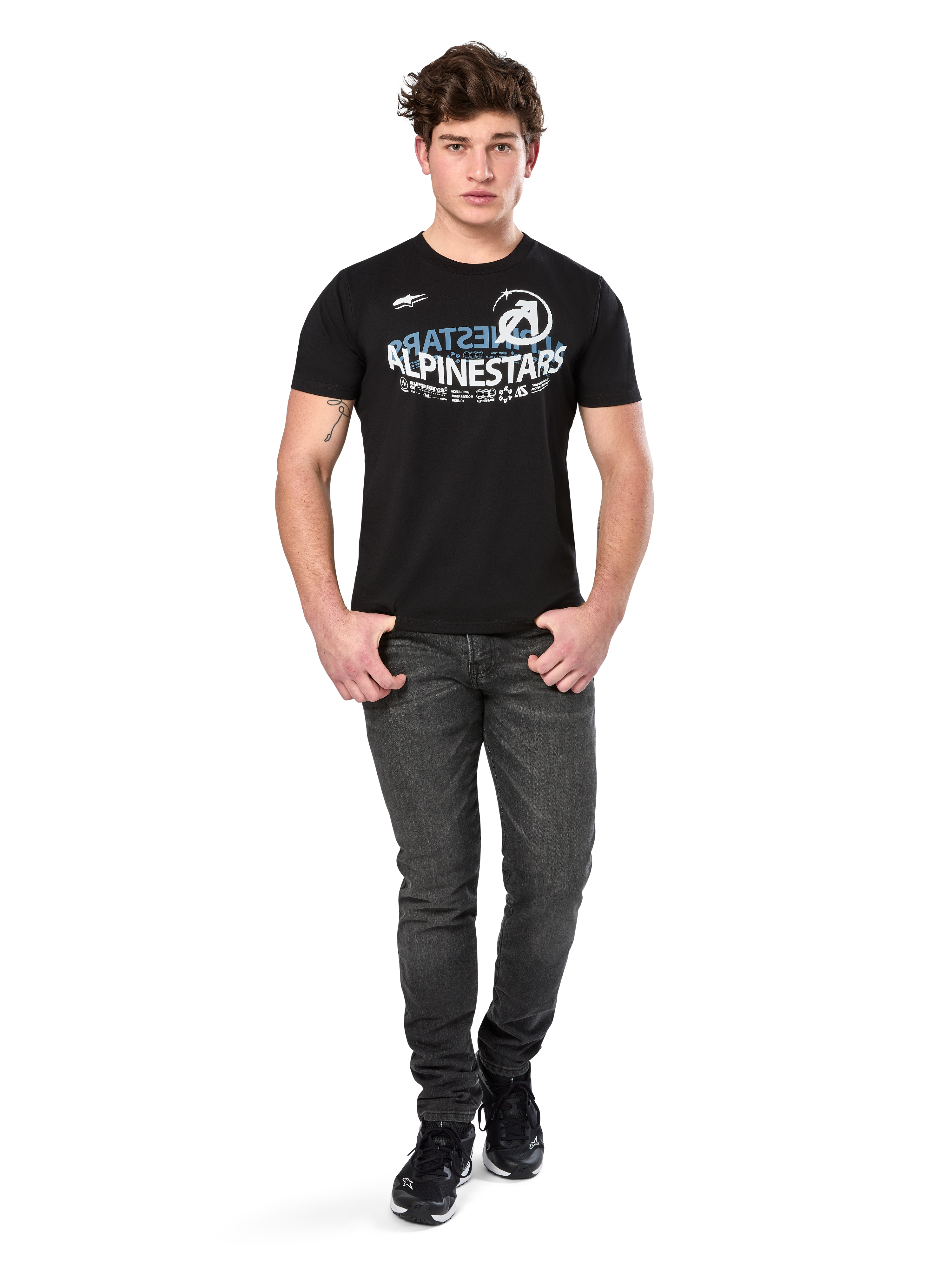 Alpinestars Semicircle CSF Tee, maglietta a maniche corte, nera, grafica curva bianca e azzurra sul petto, indossata da un modello con jeans grigio scuro e sneakers nere, streetwear casual da motorsport