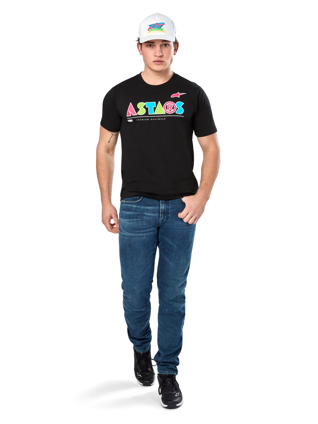 Modello maschile che indossa la maglietta Alpinestars Cereal CSF, T-shirt nera a maniche corte con logo ASTARS geometrico colorato, abbinata a jeans blu e cappellino bianco, streetwear casual ispirato al motorsport