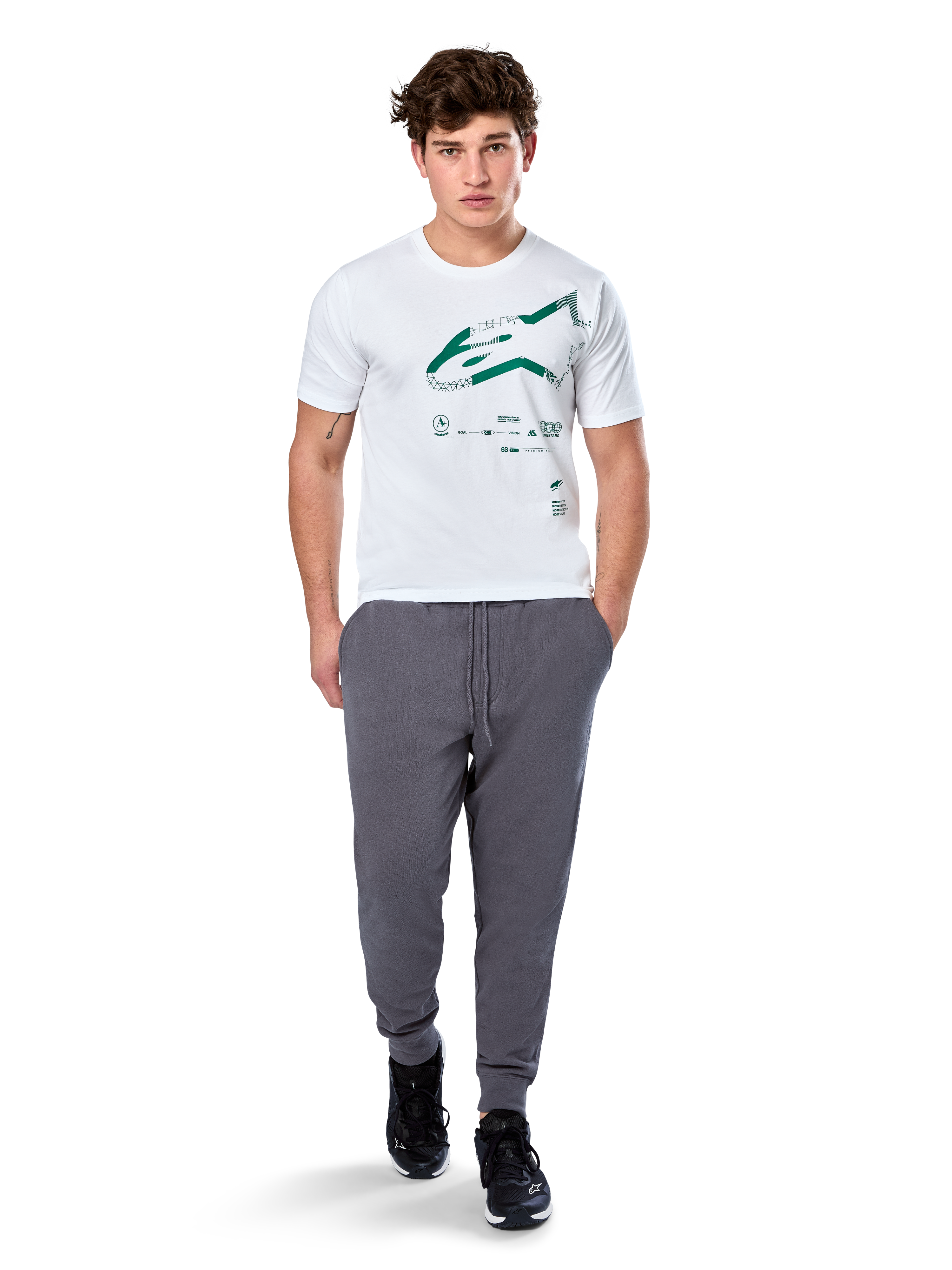 Alpinestars Geografica CSF Tee, maglietta a maniche corte, bianco, logo Astars verde con grafica multi-tech geografica, indossata con pantaloni sportivi grigi e sneakers nere, streetwear casual ispirato al motorsport