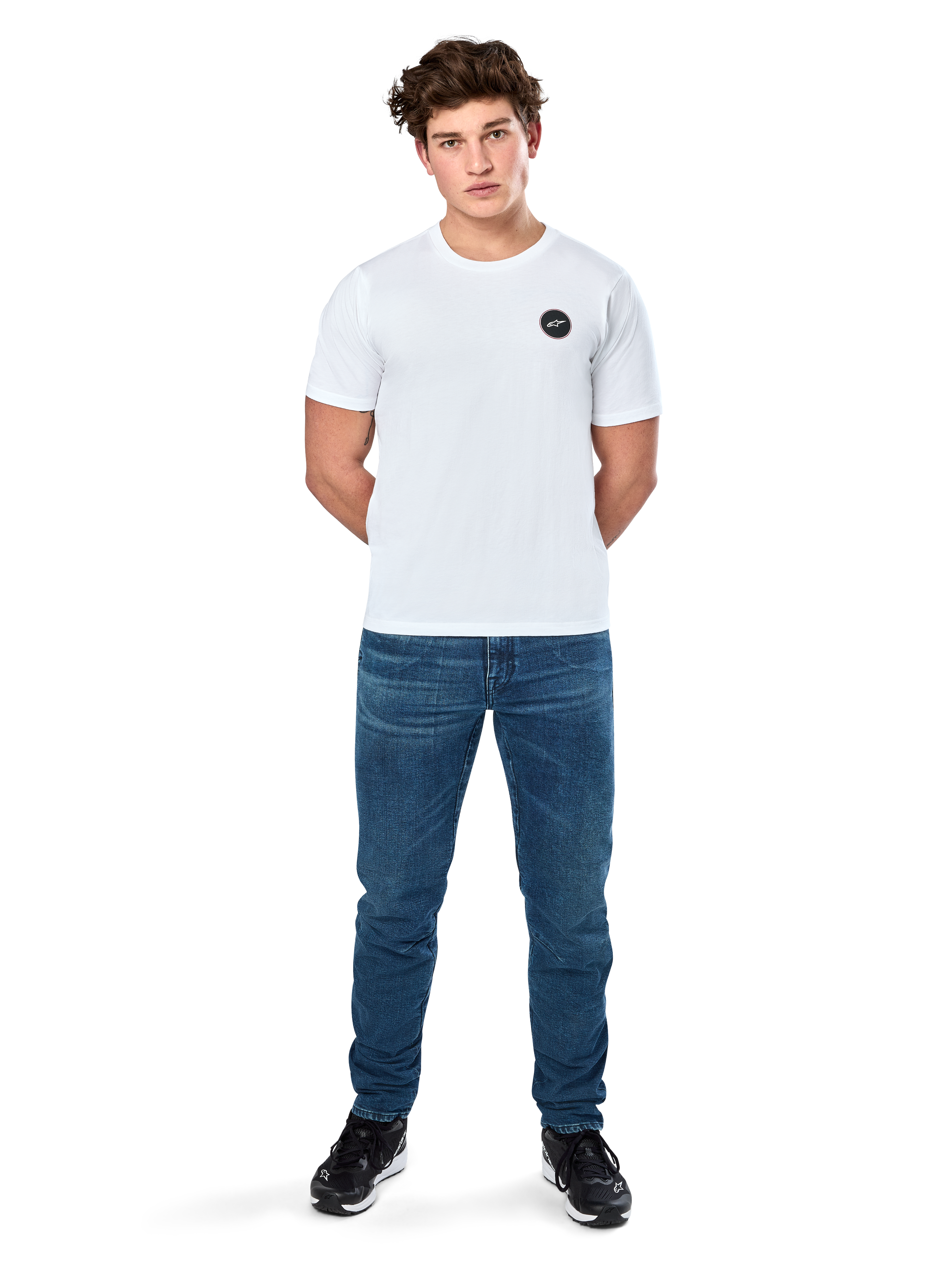 Alpinestars Dot Carbon Csf Tee, t-shirt a maniche corte, bianca, logo circolare Astars con effetto fibra di carbonio, abbigliamento casual motorsport, indossata da un modello con jeans blu e sneakers nere