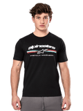 Alpinestars Prevail CSF Tee, maglietta nera a maniche corte indossata da un modello, con logo bianco, striscia tricolore e grafica "PREMIUM RACEWEAR", streetwear casual motorsport