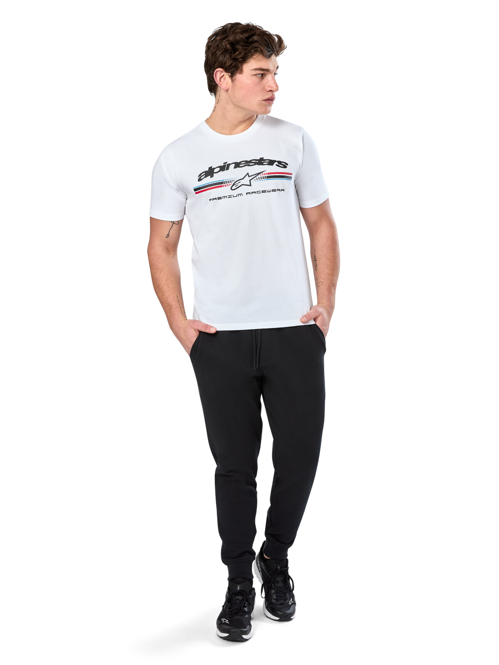 Alpinestars T-shirt Prevail CSF, t-shirt a maniche corte, bianca, con logo a strisce tricolore stile paddock anteriore e marchio Alpinestars, indossata da un modello con pantaloni sportivi neri e sneaker nere, streetwear casual da motorsport