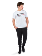 Alpinestars T-shirt Prevail CSF, t-shirt a maniche corte, bianca, con logo a strisce tricolore stile paddock anteriore e marchio Alpinestars, indossata da un modello con pantaloni sportivi neri e sneaker nere, streetwear casual da motorsport